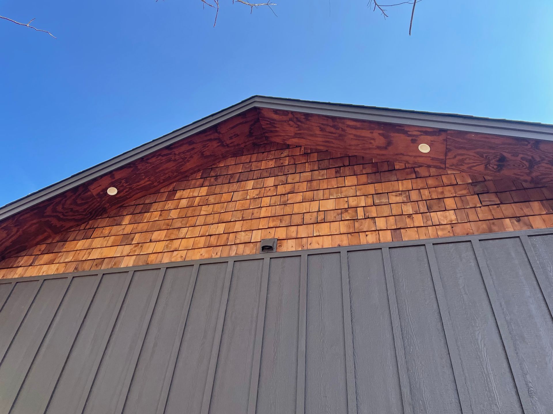 Wood-shingled gable above a gray metal roof against a blue sky