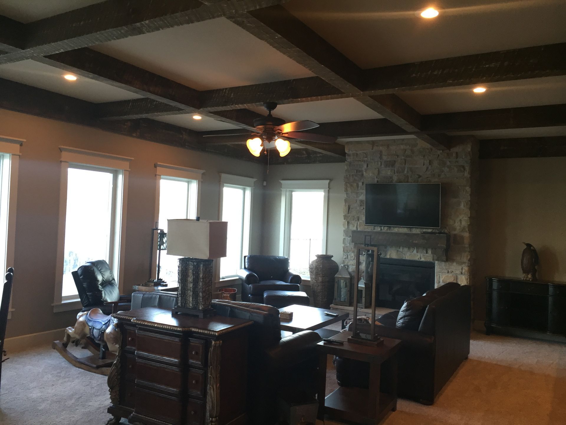 Spacious living room with leather furniture, stone fireplace, ceiling fan, and large windows