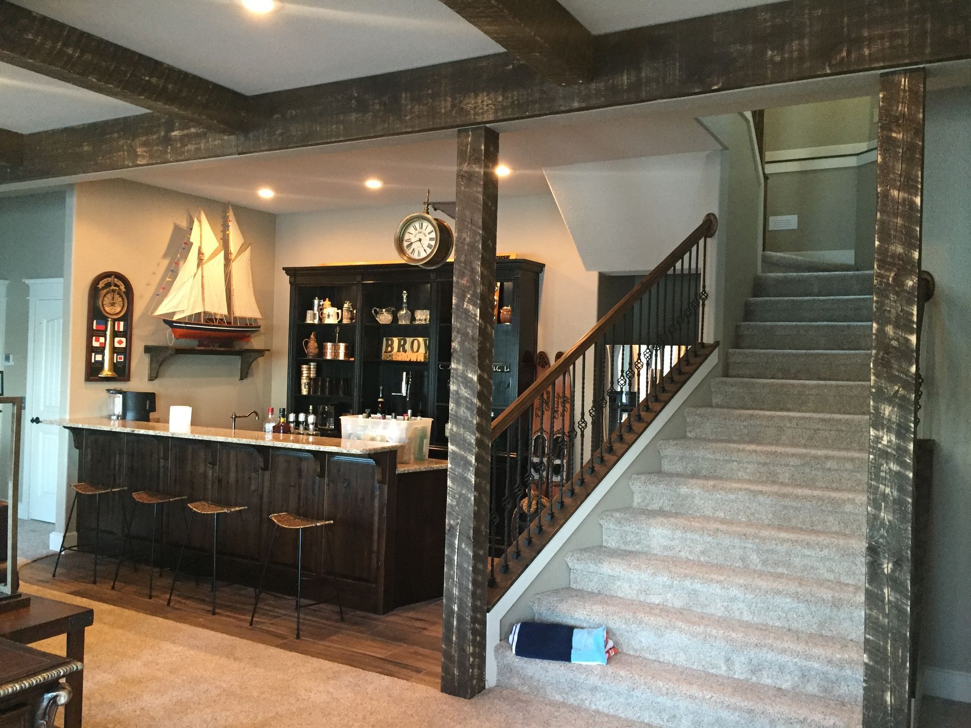 Basement bar area with stairs, dark wood counter, shelves, and a model sailboat display