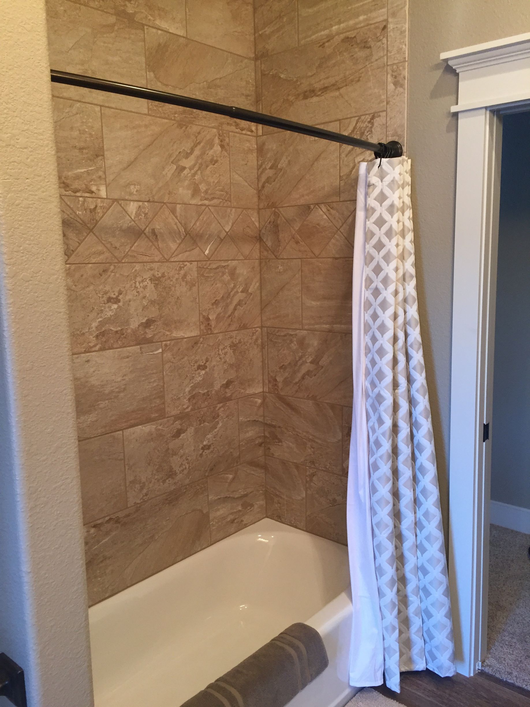 Bathtub shower with beige tile walls and a patterned shower curtain partially closed