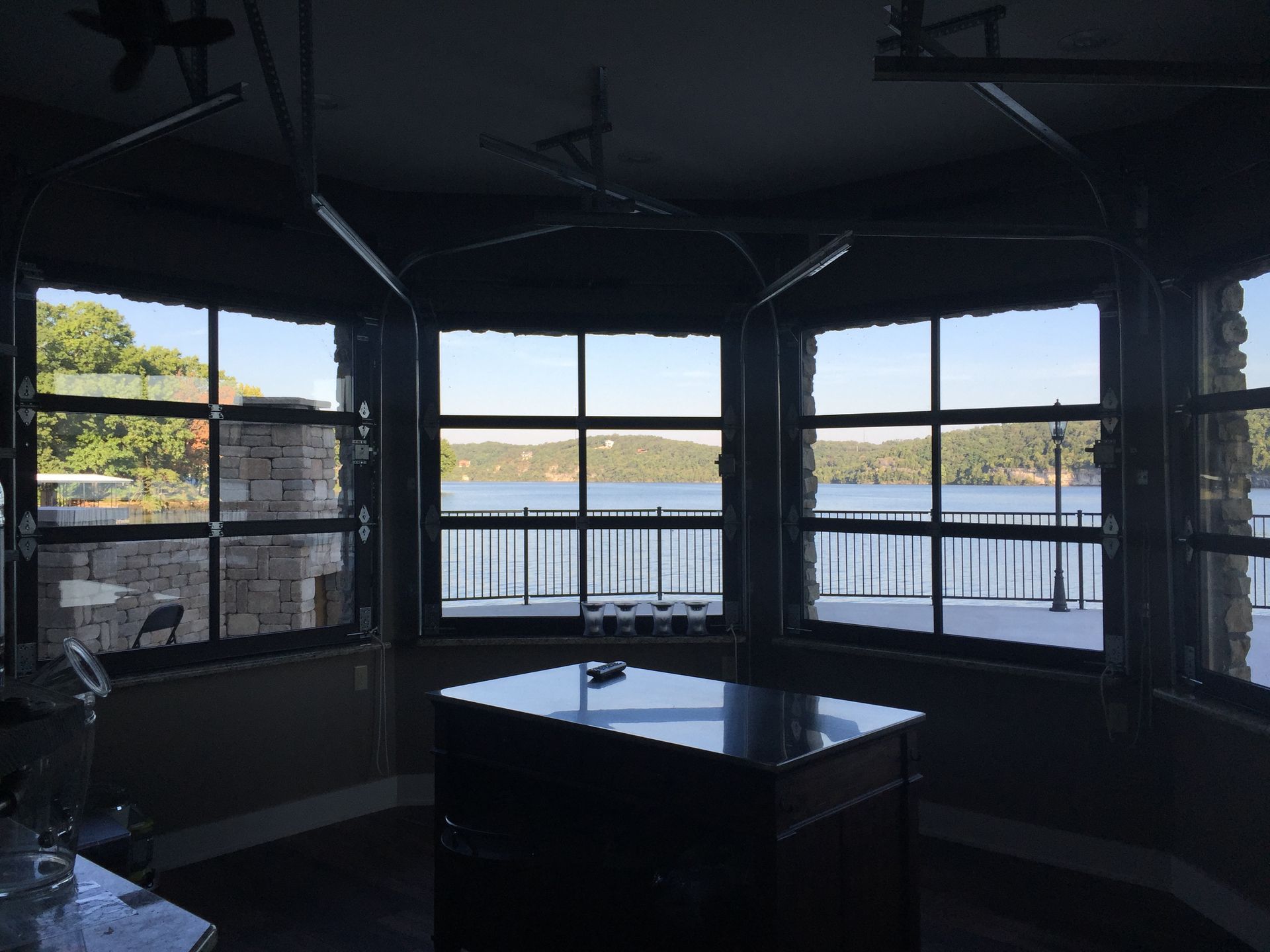 Dark room with large bay windows overlooking a bright waterfront and a black table in the center