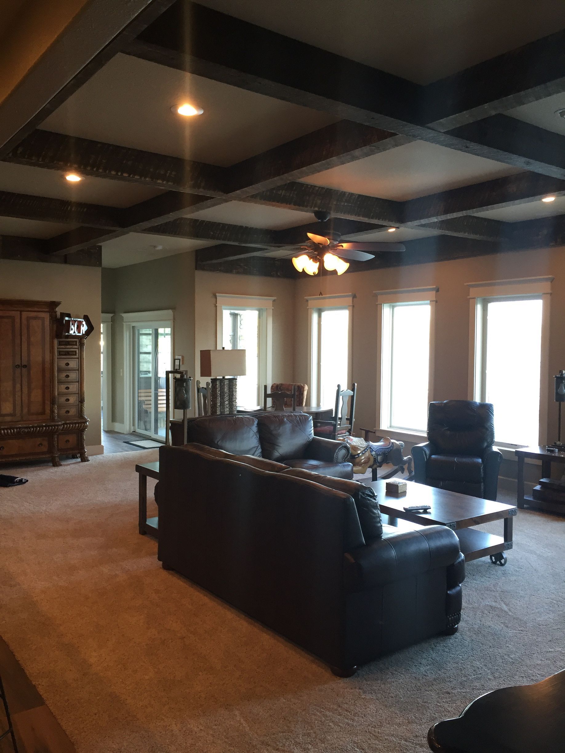 Spacious living room with dark leather sofas, wood cabinetry, and large windows under a coffered ceiling.