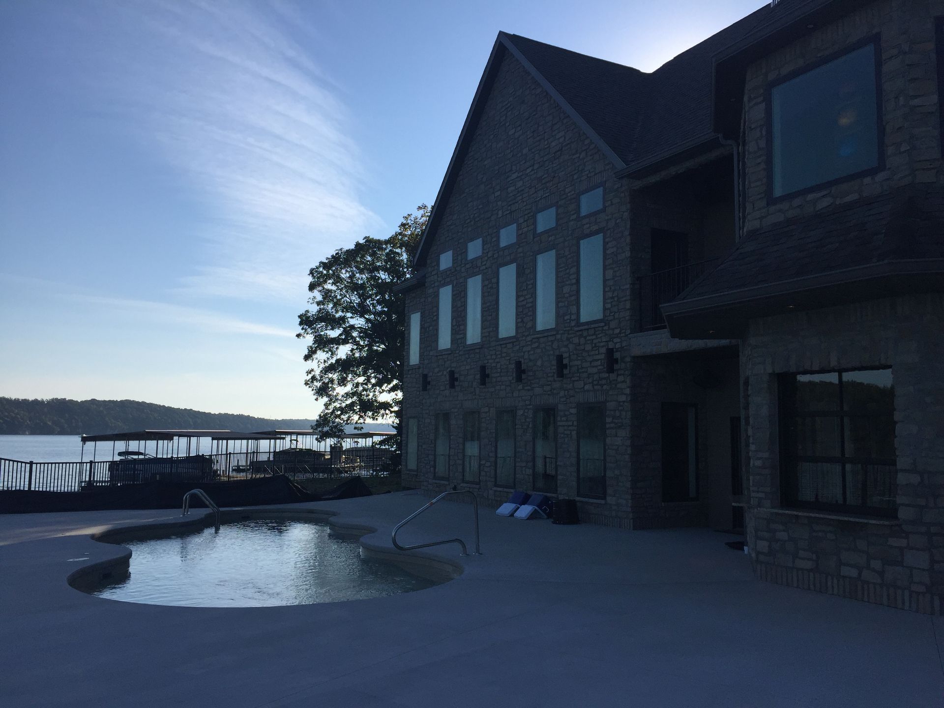 Stone lakeside house with a pool and deck at sunset