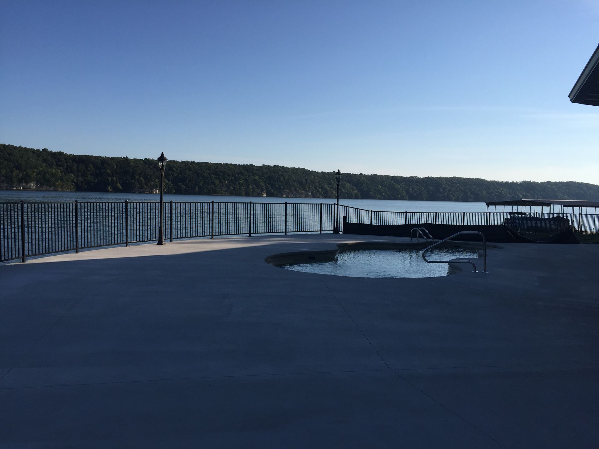 Riverside deck with metal railing, lounge chairs, and calm water under a clear blue sky