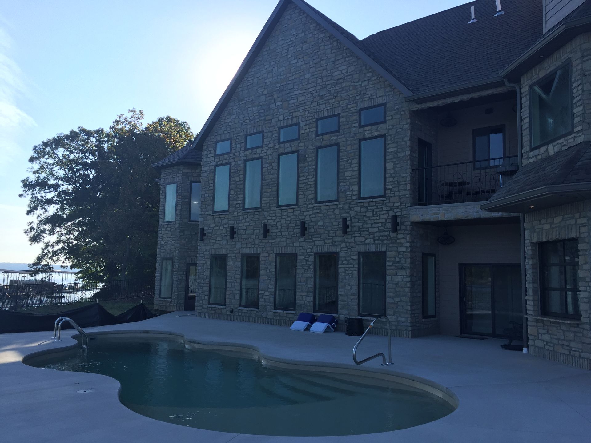Stone house patio with a kidney-shaped pool and lounge chairs by the water