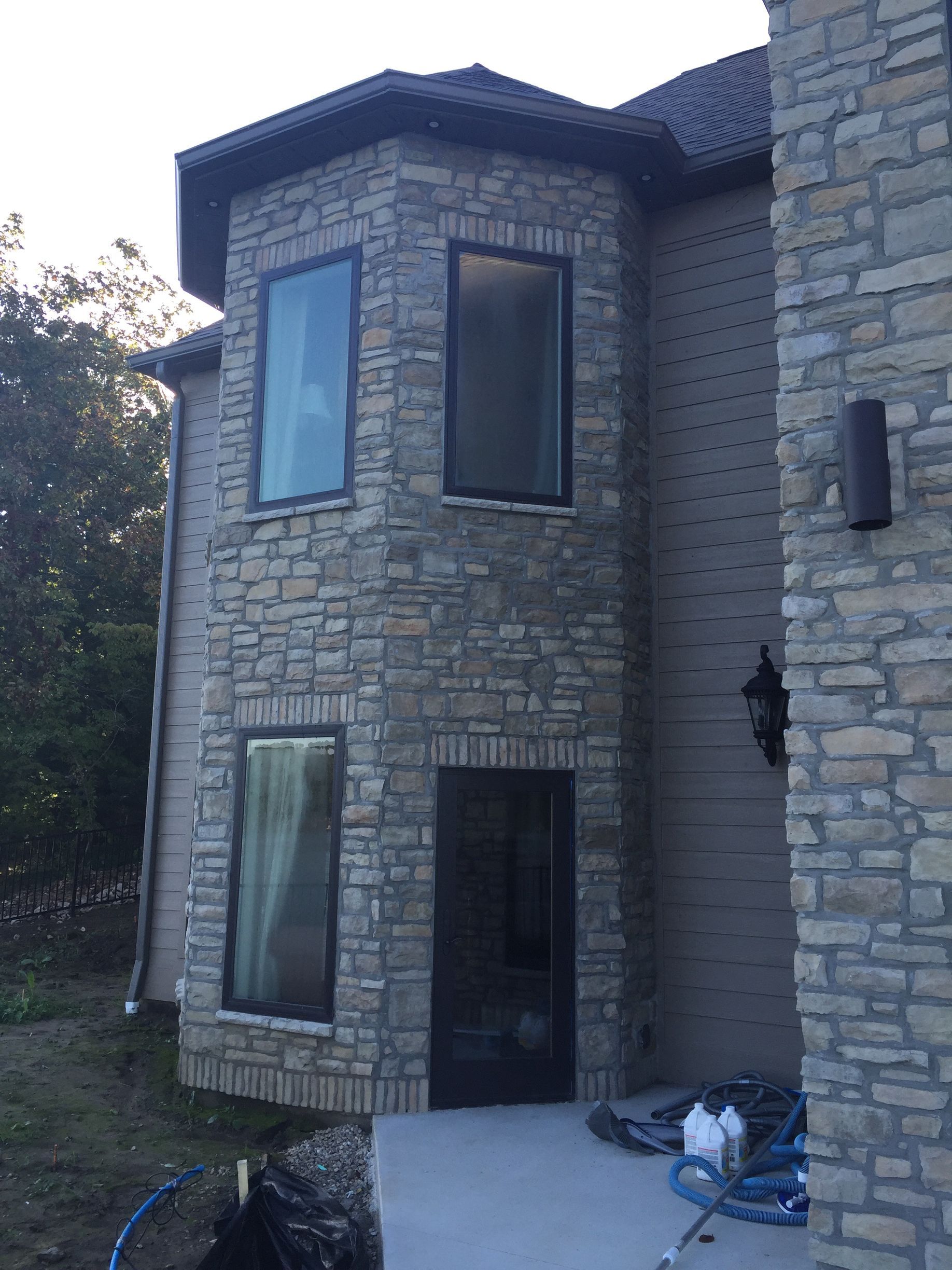 Stone two-story house with bay windows and a dark front door, viewed from the driveway
