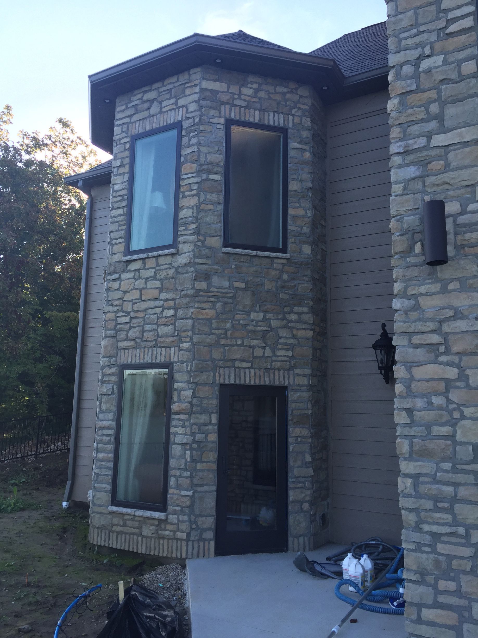 Two-story stone house with tall windows and a dark front door under construction.