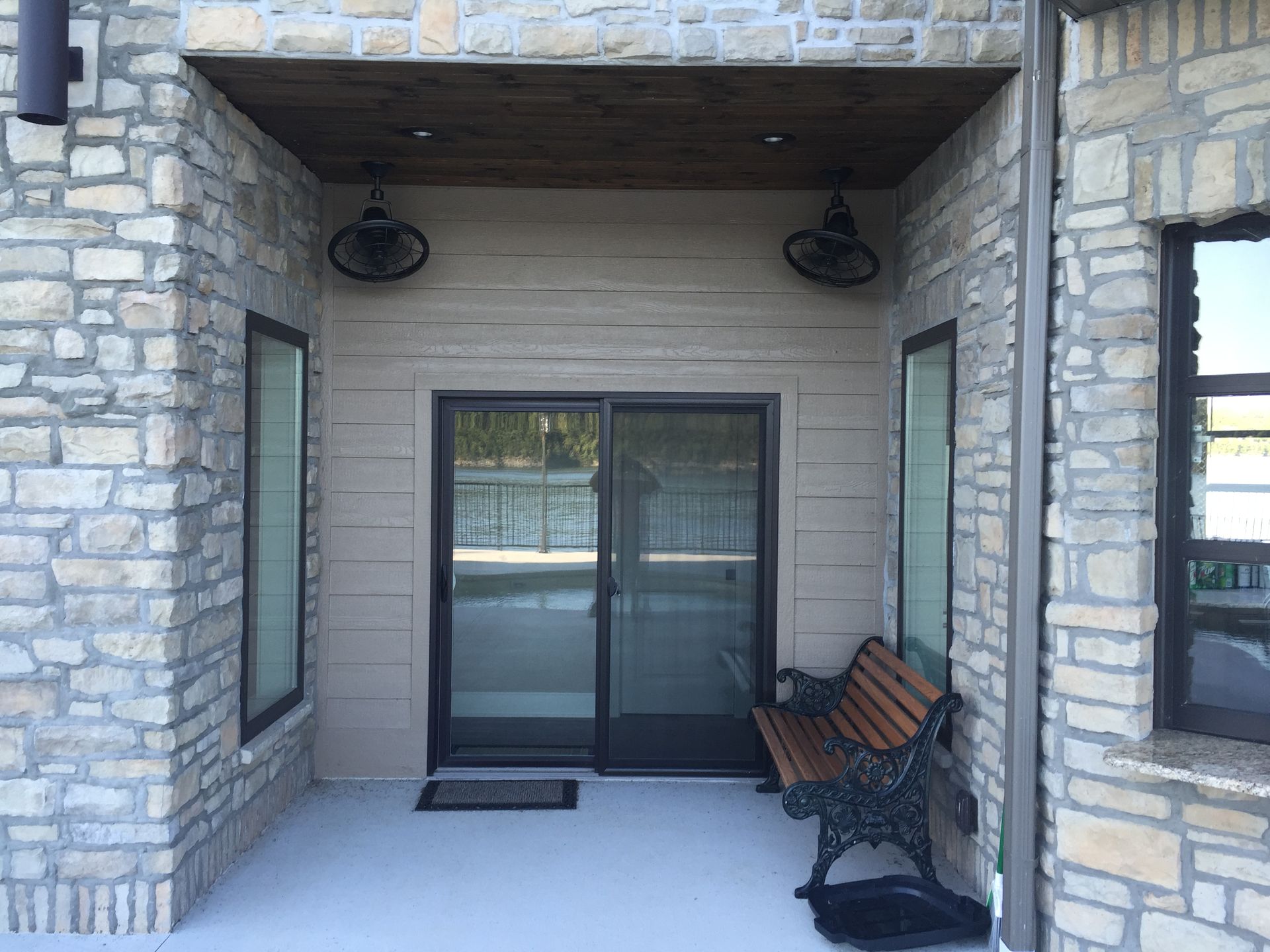 Stone building entrance with sliding glass doors, wall lamps, and a bench under a covered porch