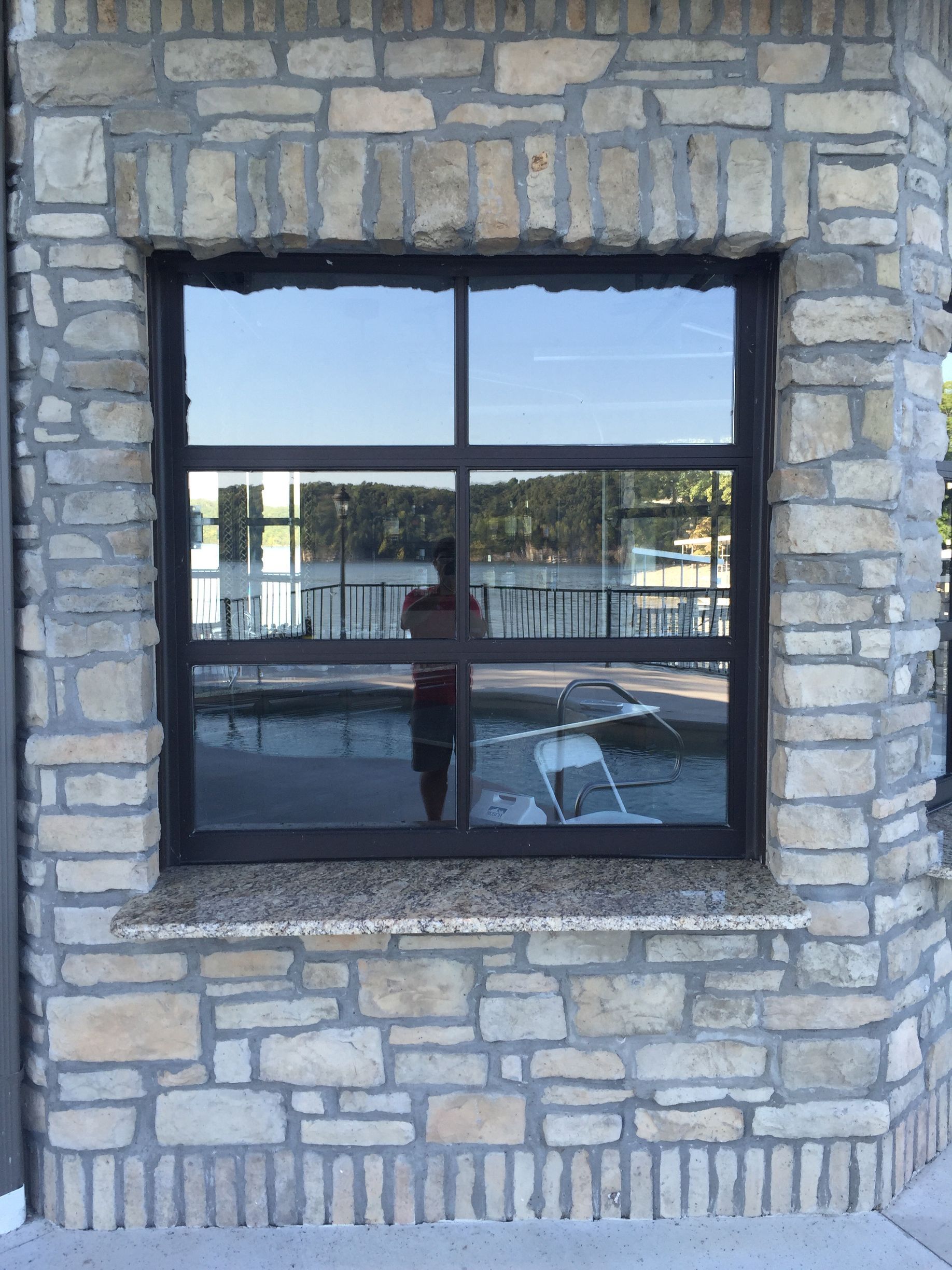 Stone building wall with a black-framed window reflecting a balcony and water beyond