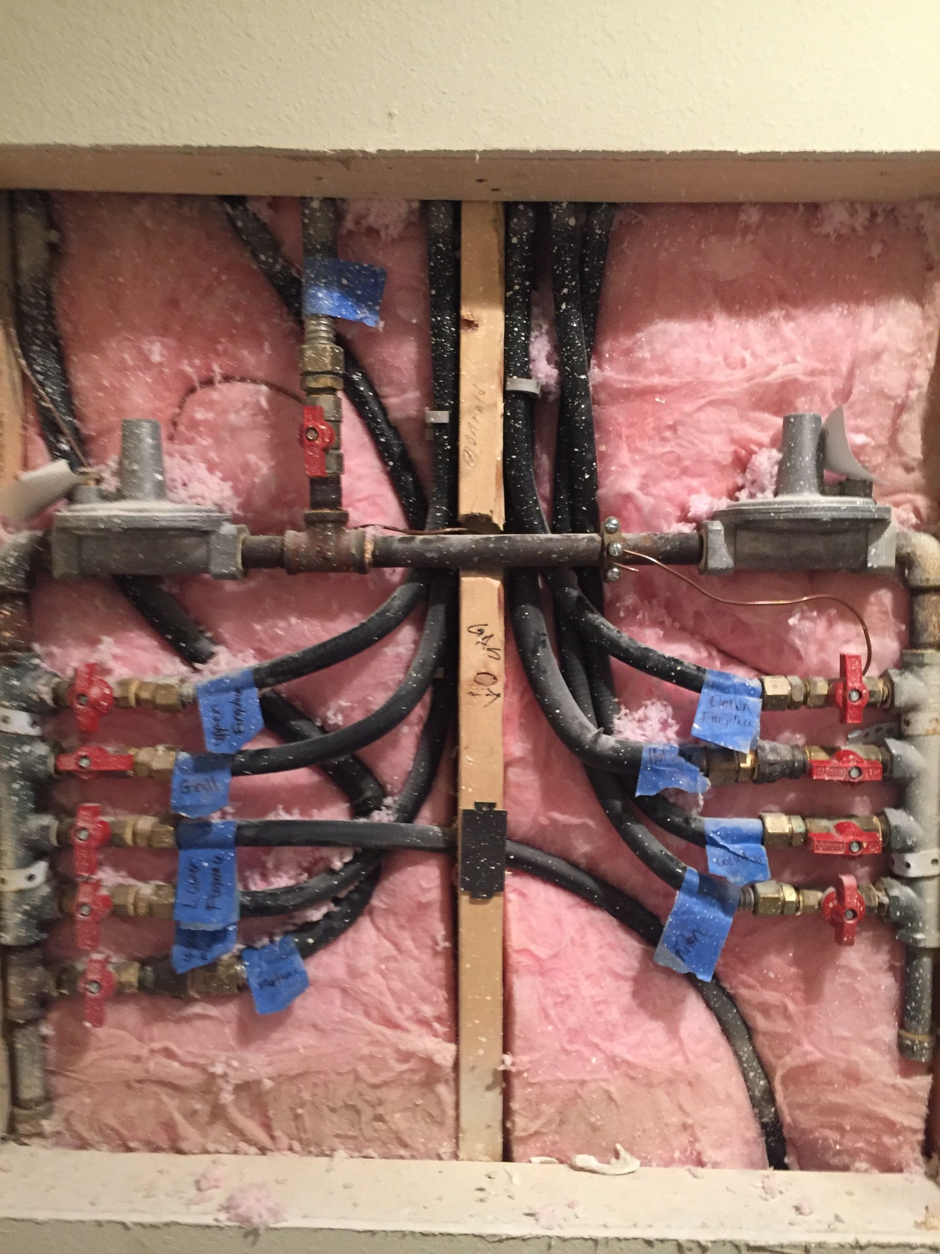 Open electrical panel with pink insulation, black cables, blue wire connectors, and red valve fittings