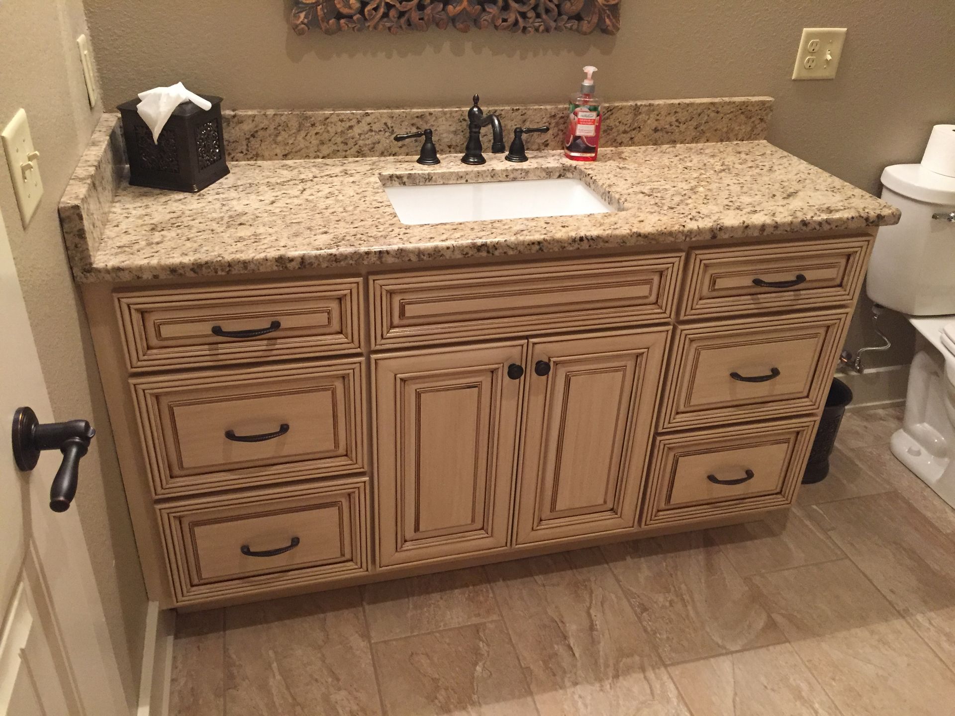 Wooden bathroom vanity with speckled granite countertop, sink, mirror, and drawers.