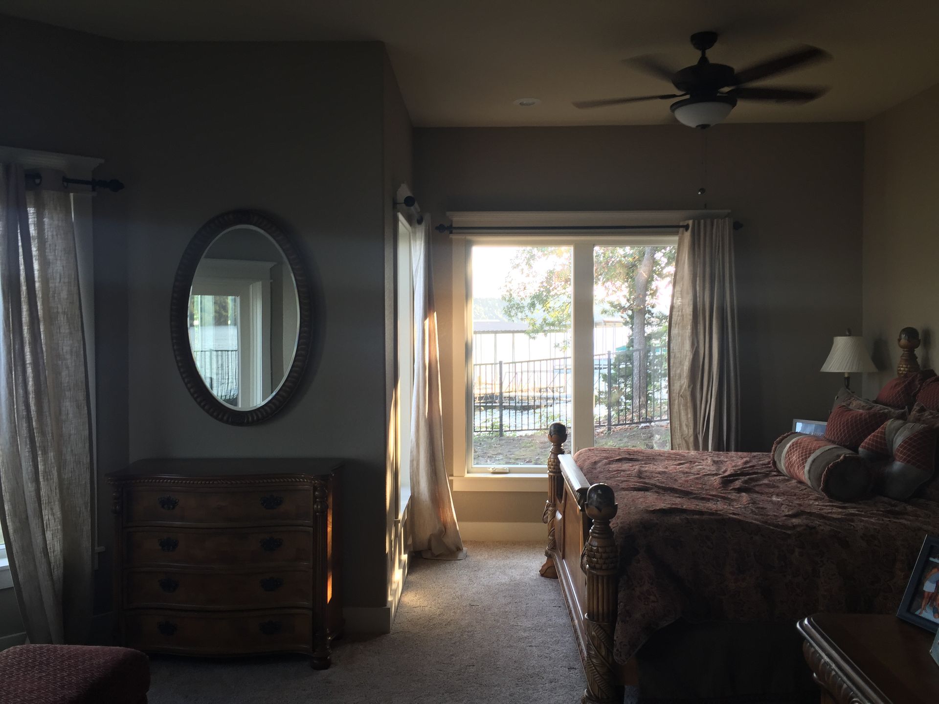 Bedroom with a bed, dresser, oval mirror, and sliding glass doors letting in daylight.