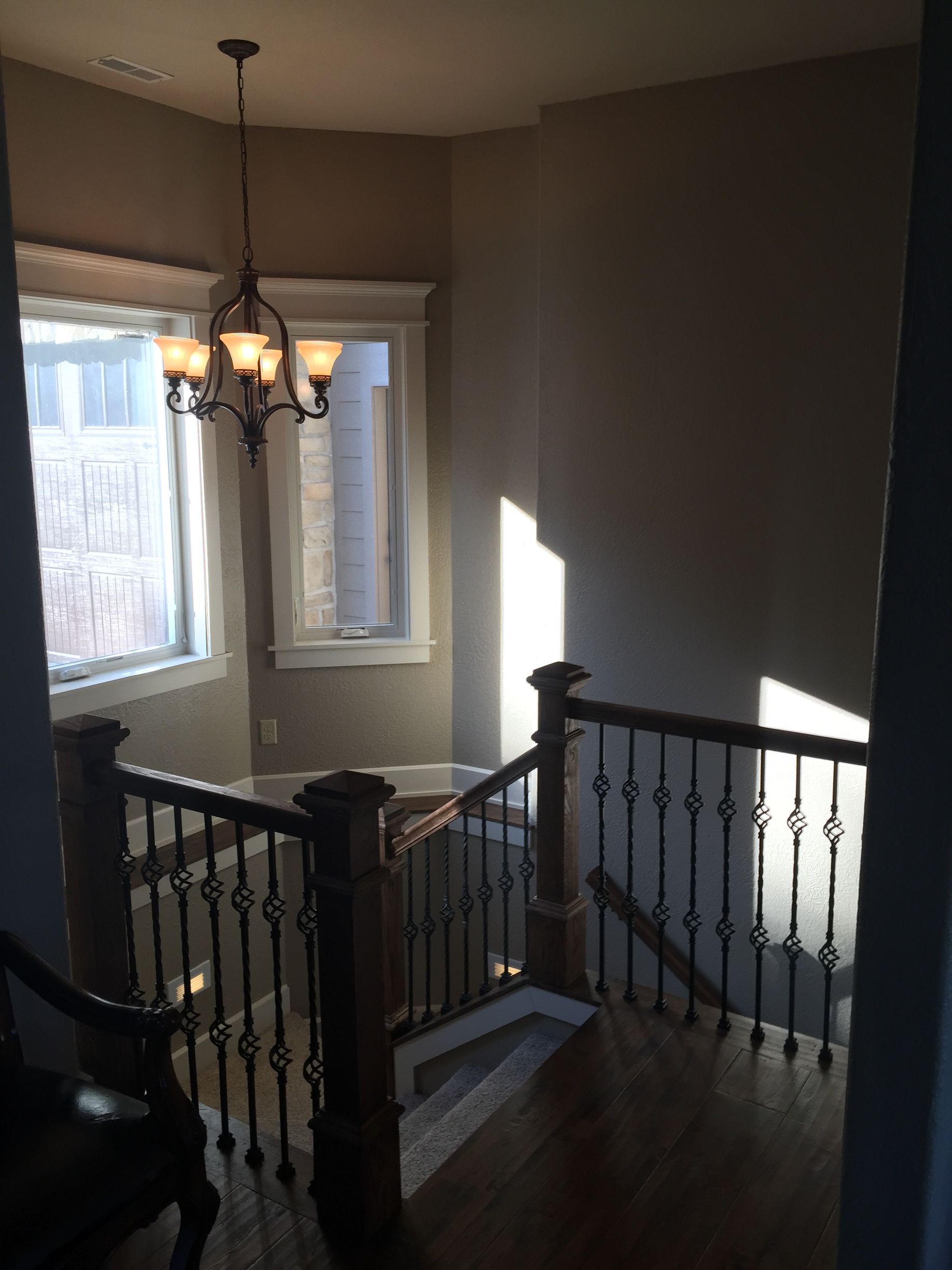 Stair landing with dark wood banister, chandelier, and sunlight streaming through windows.