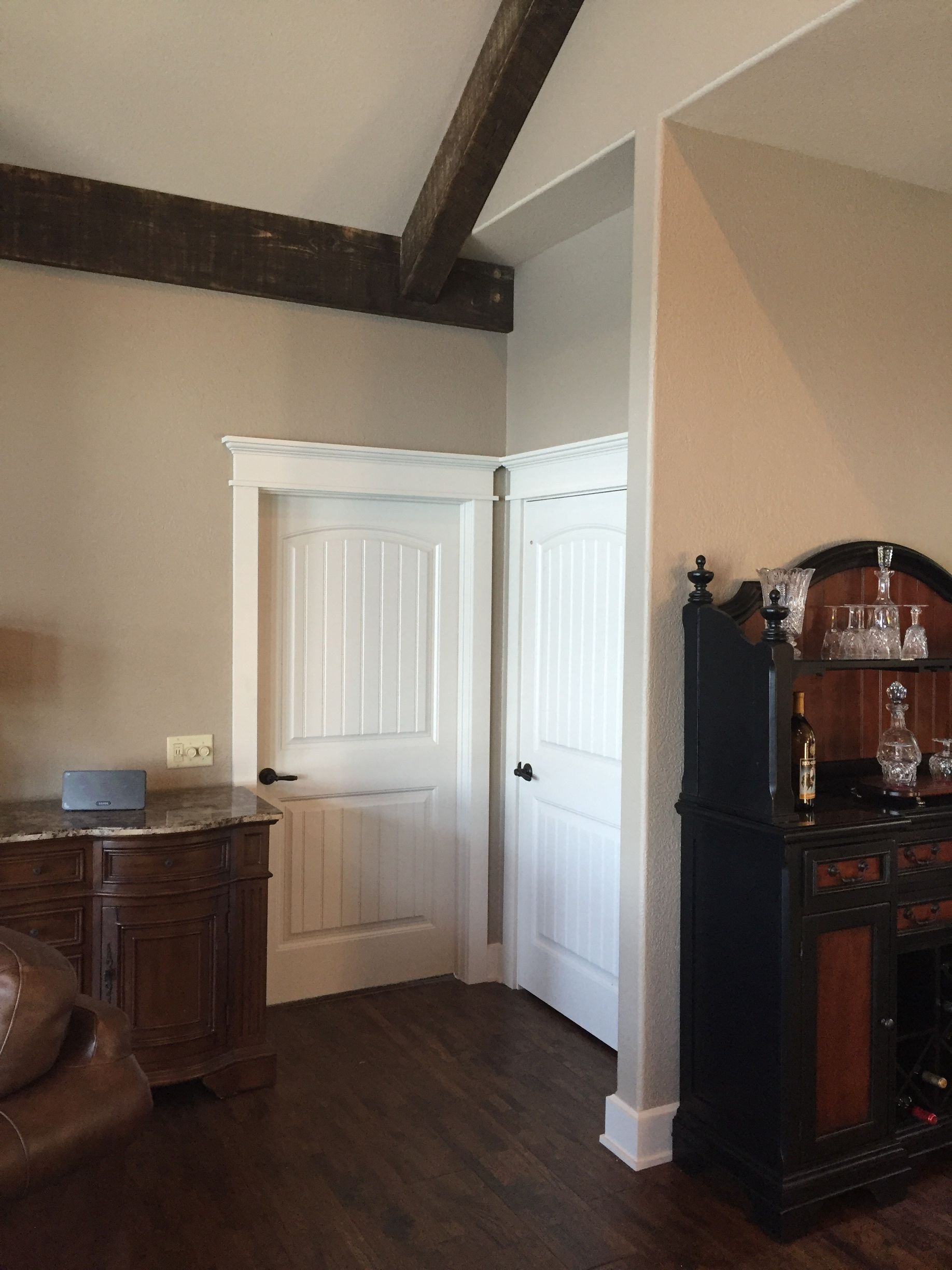 Corner of a living room with dark wood floors, white walls, and a black cabinet beside a white door.