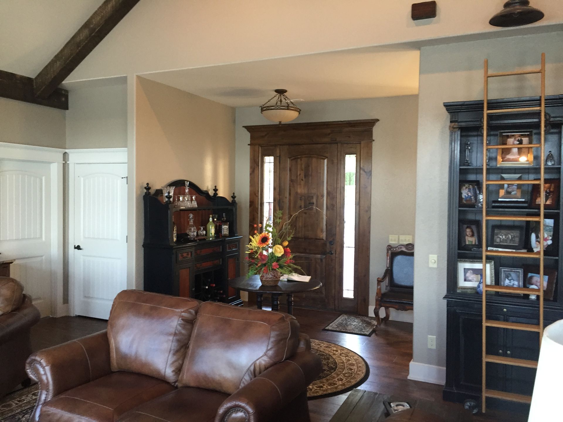 Living room with brown leather sofa, wooden front door, arched doorway, and tall shelving unit