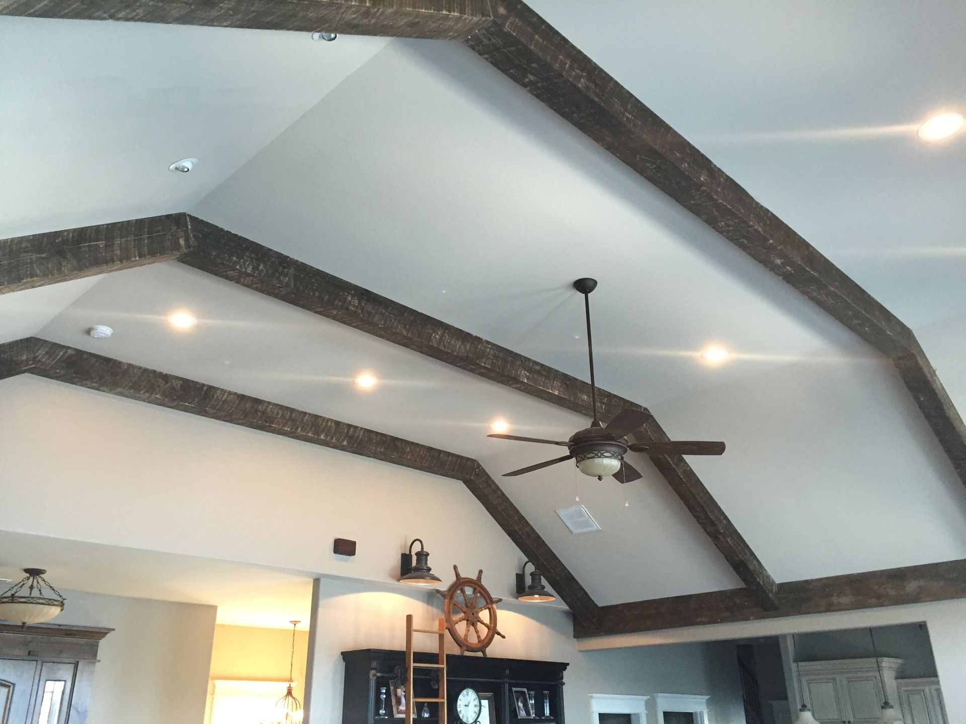 Vaulted ceiling with dark wooden beams, recessed lights, and ceiling fan in a bright room