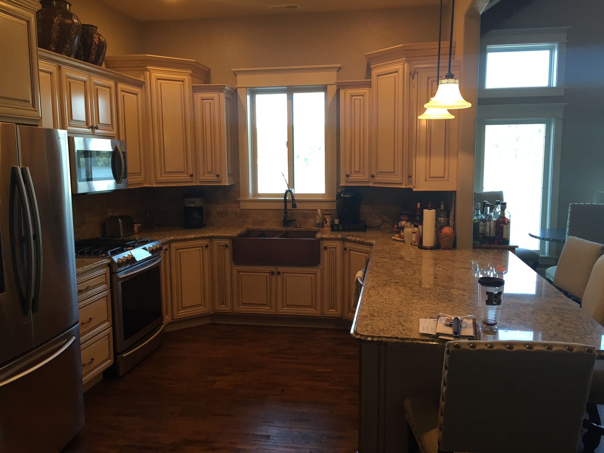 Warm-lit kitchen with stainless steel appliances, granite island, and wood cabinets around a central window.