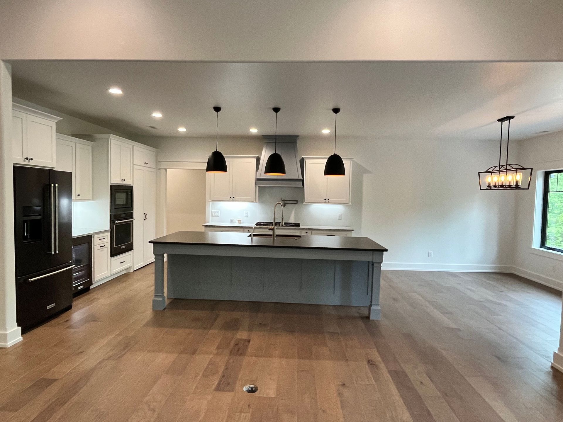 Modern open-concept kitchen with large island, white cabinets, black pendant lights, and hardwood floors