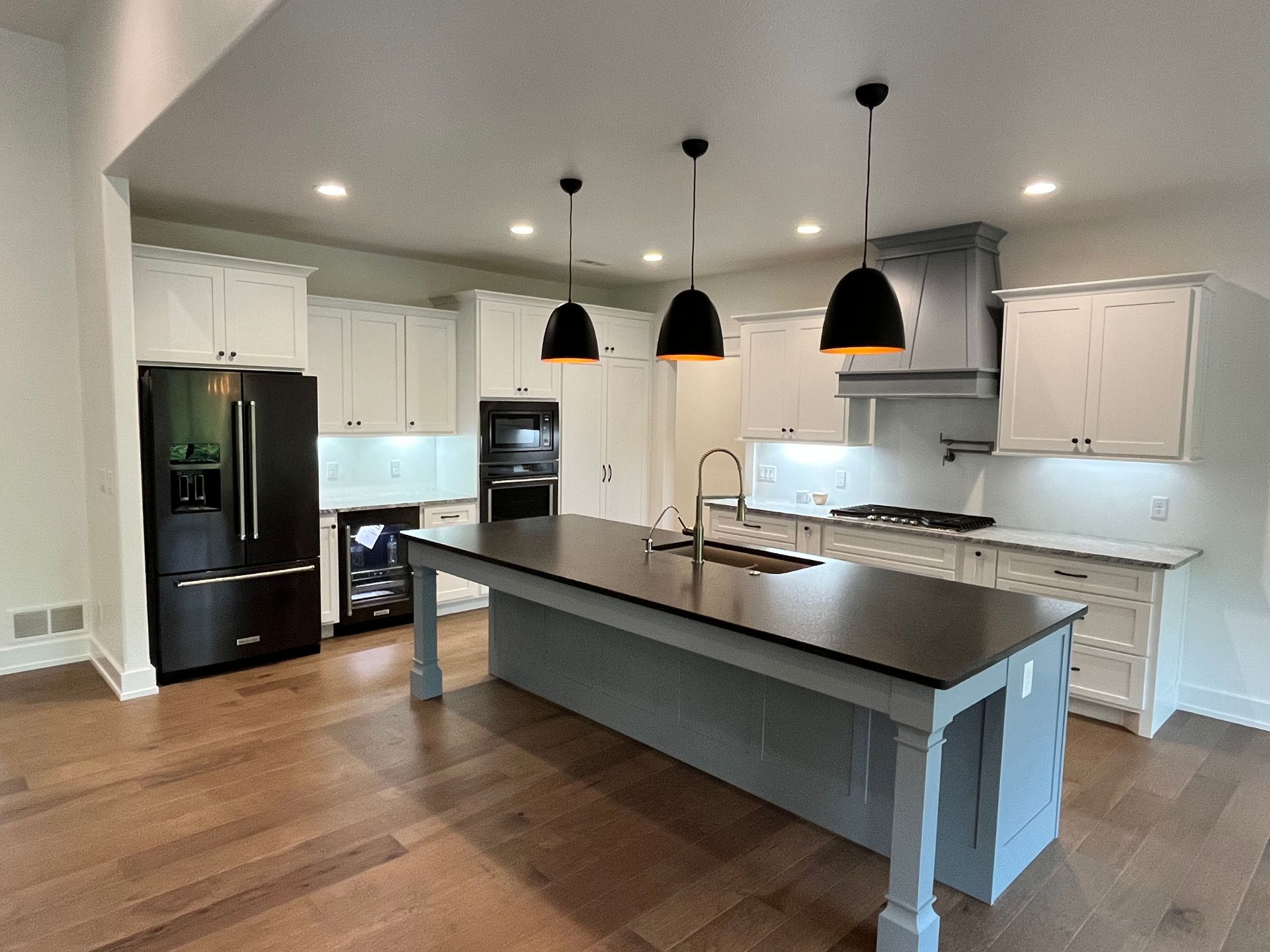 Modern kitchen with large island, black pendant lights, white cabinets, and hardwood floors