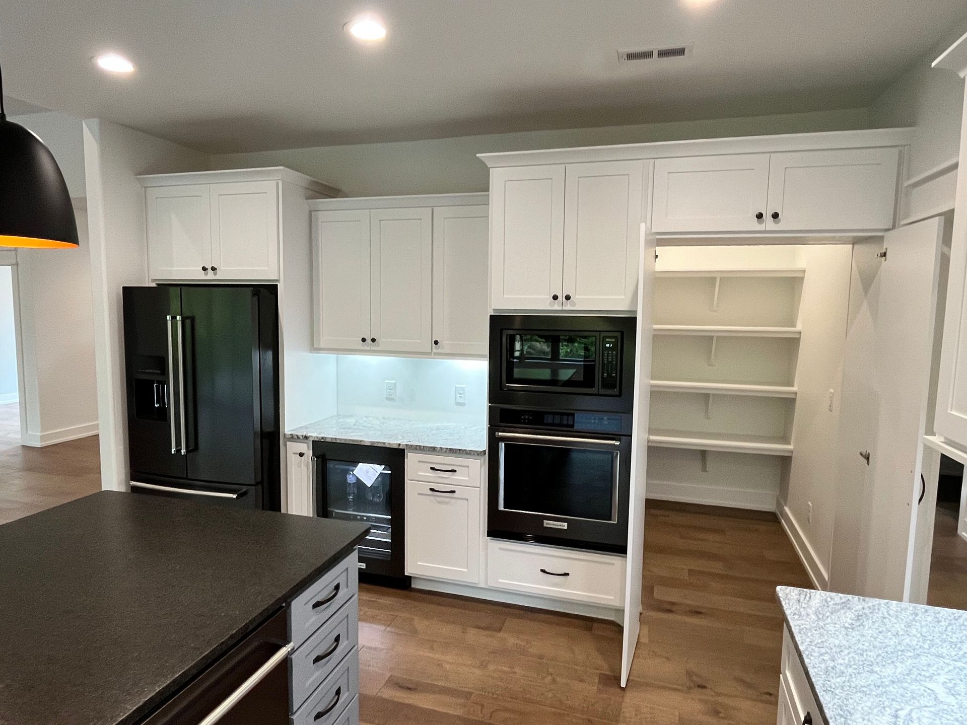 Bright white kitchen with black appliances, island countertop, and open pantry shelving