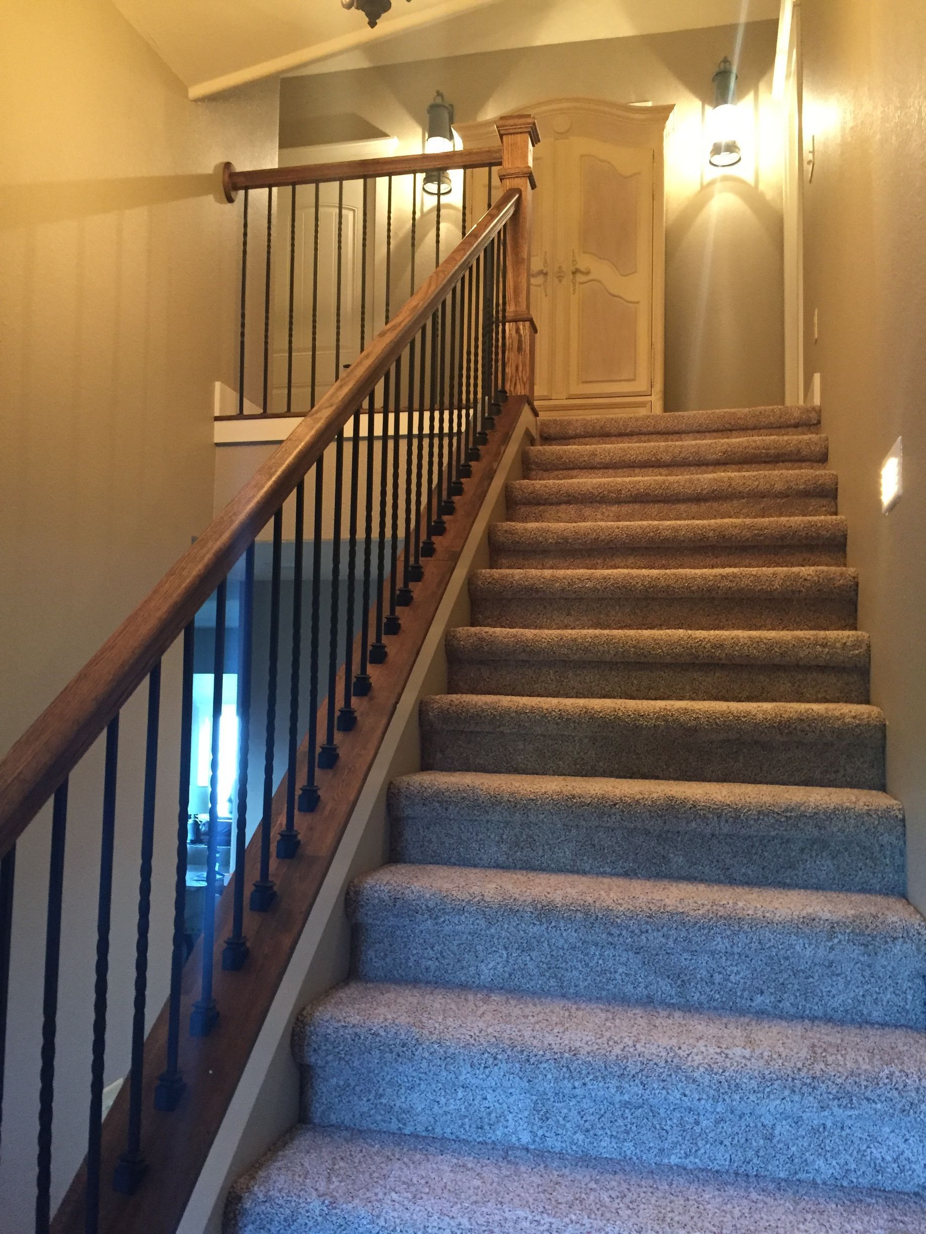 Carpeted indoor staircase with wooden handrail and warm wall sconces in a hallway