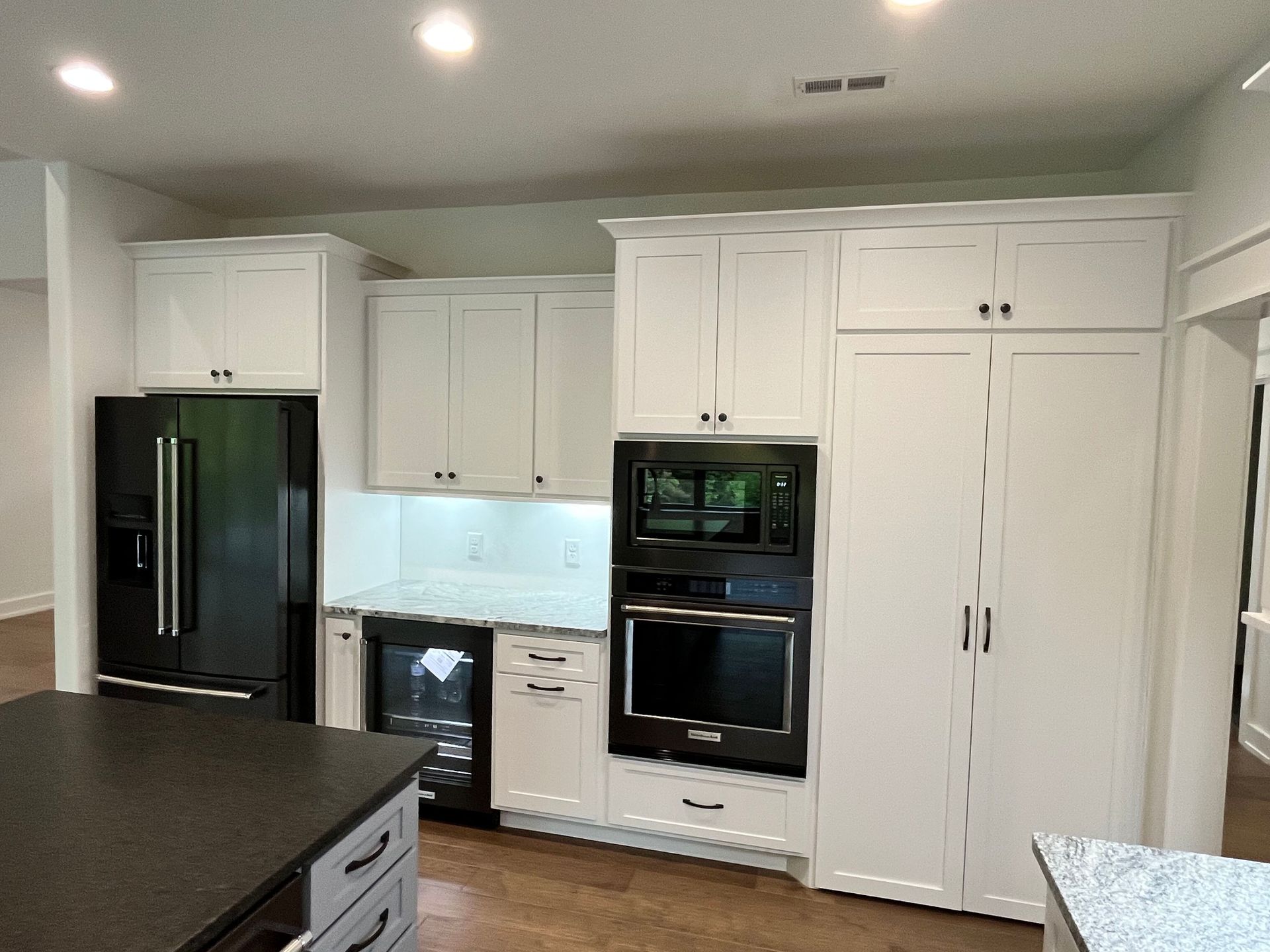 Bright white kitchen with stainless steel appliances, black countertops, and a dishwasher under the sink.