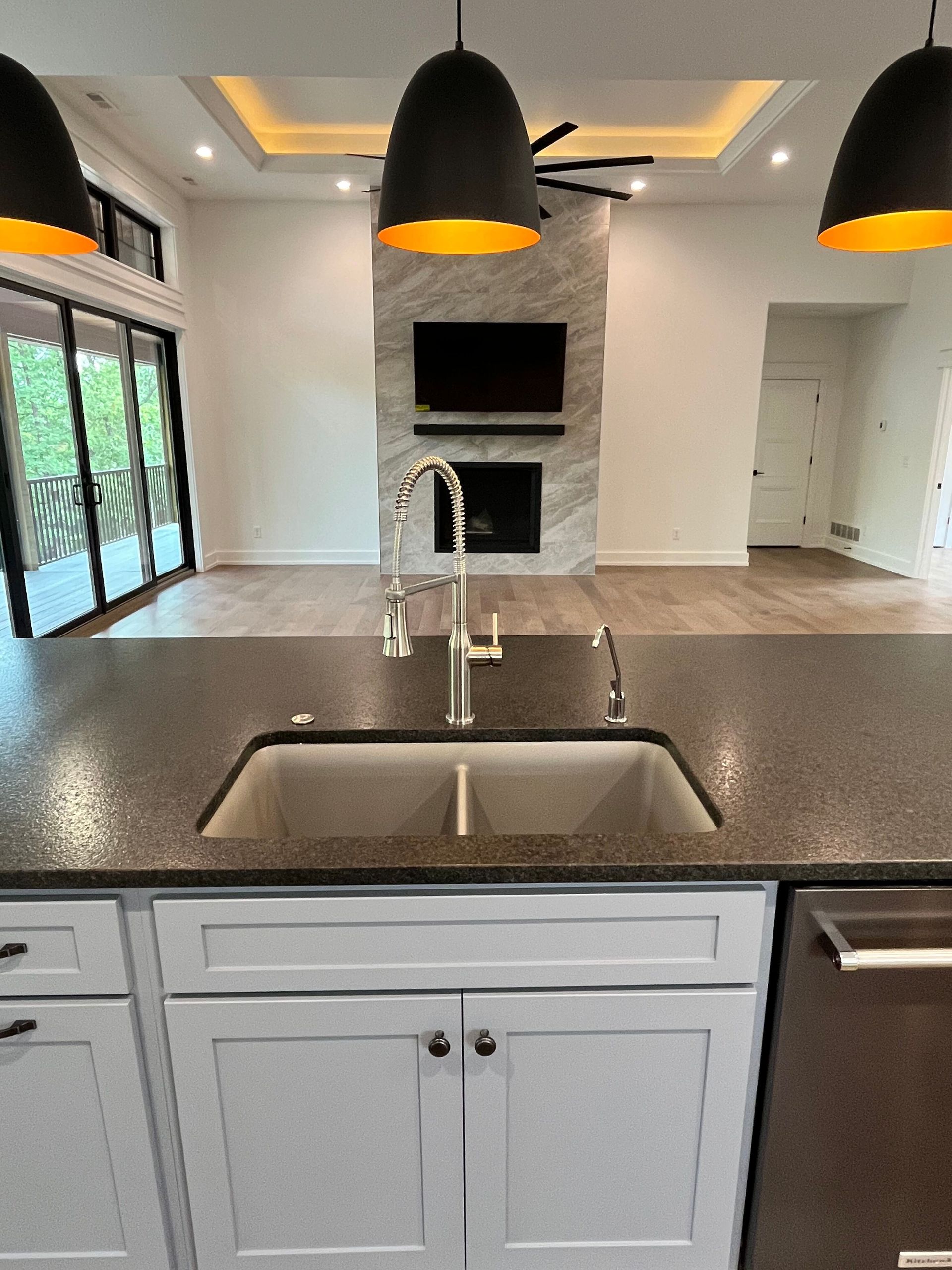 Modern kitchen with island sink, dark countertop, pendant lights, white cabinets, and fireplace in the background