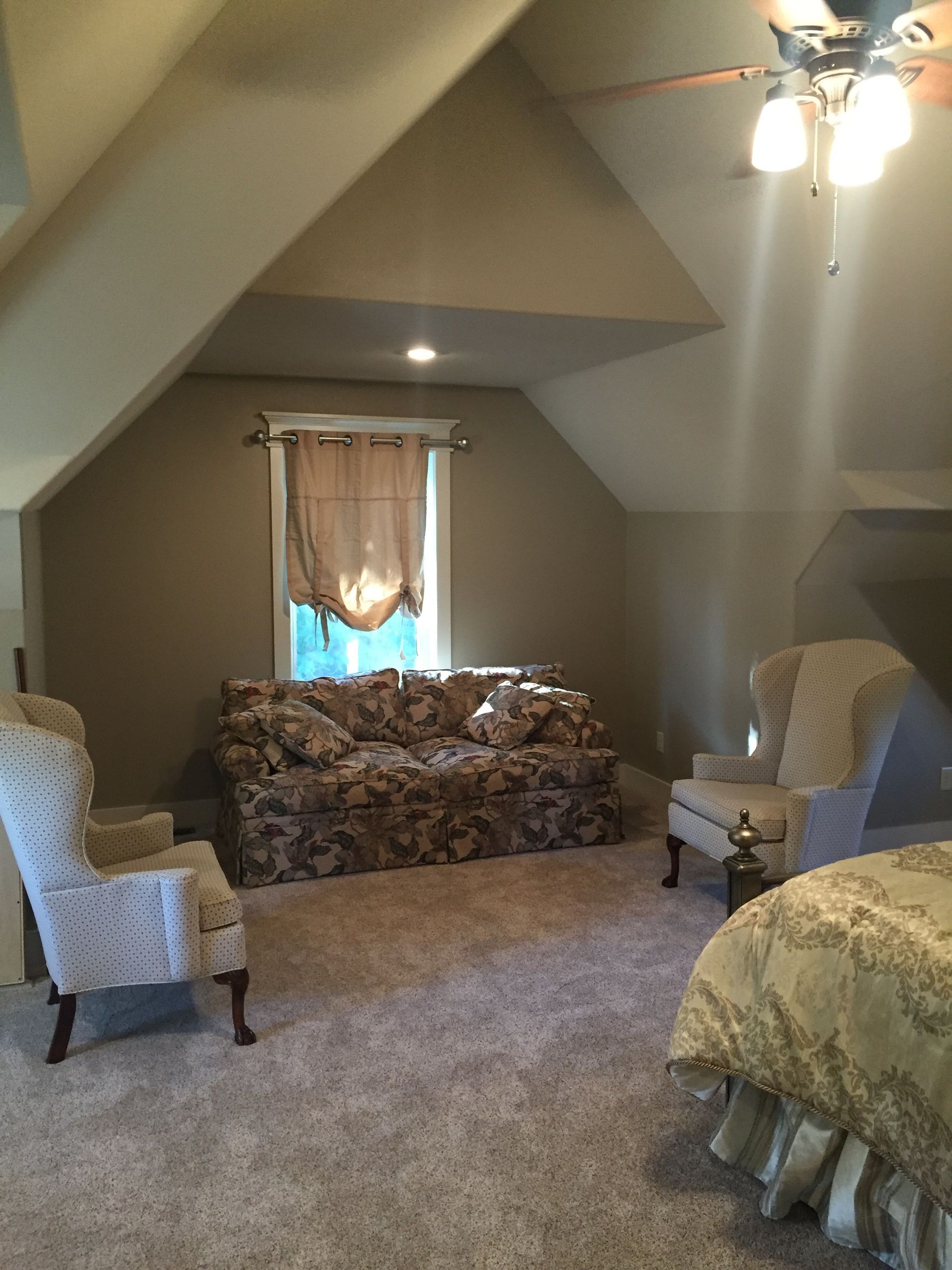 Attic bedroom with carpeted floor, floral sofa, armchairs, bed, and a small window under a sloped ceiling
