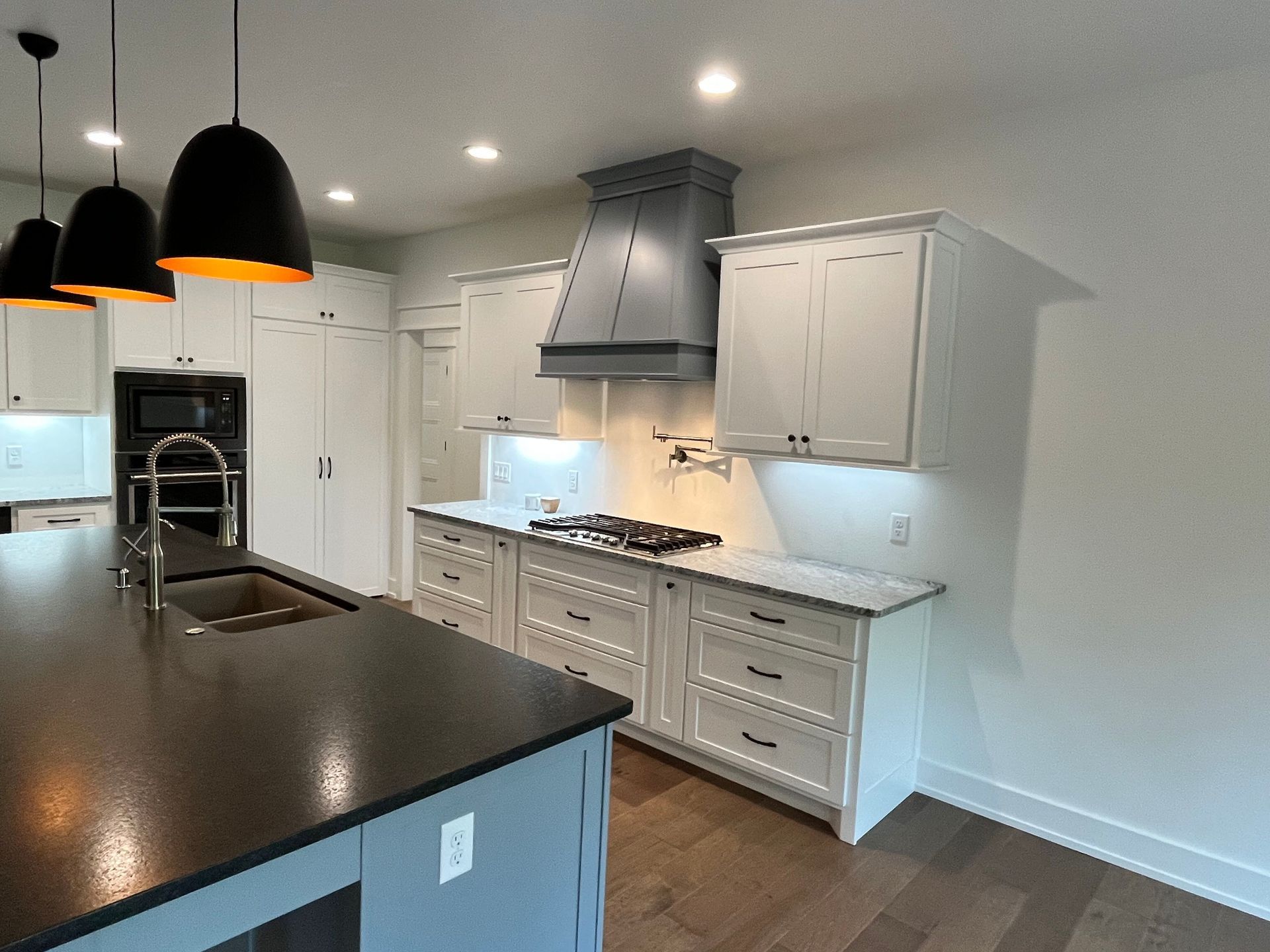 Bright modern kitchen with white cabinets, dark countertops, island, pendant lights, and stainless steel appliances