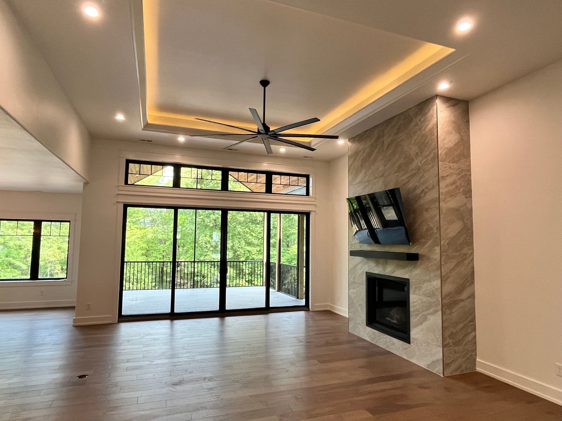 Empty modern living room with fireplace, wood floors, large sliding glass doors, and ceiling fan in neutral tones