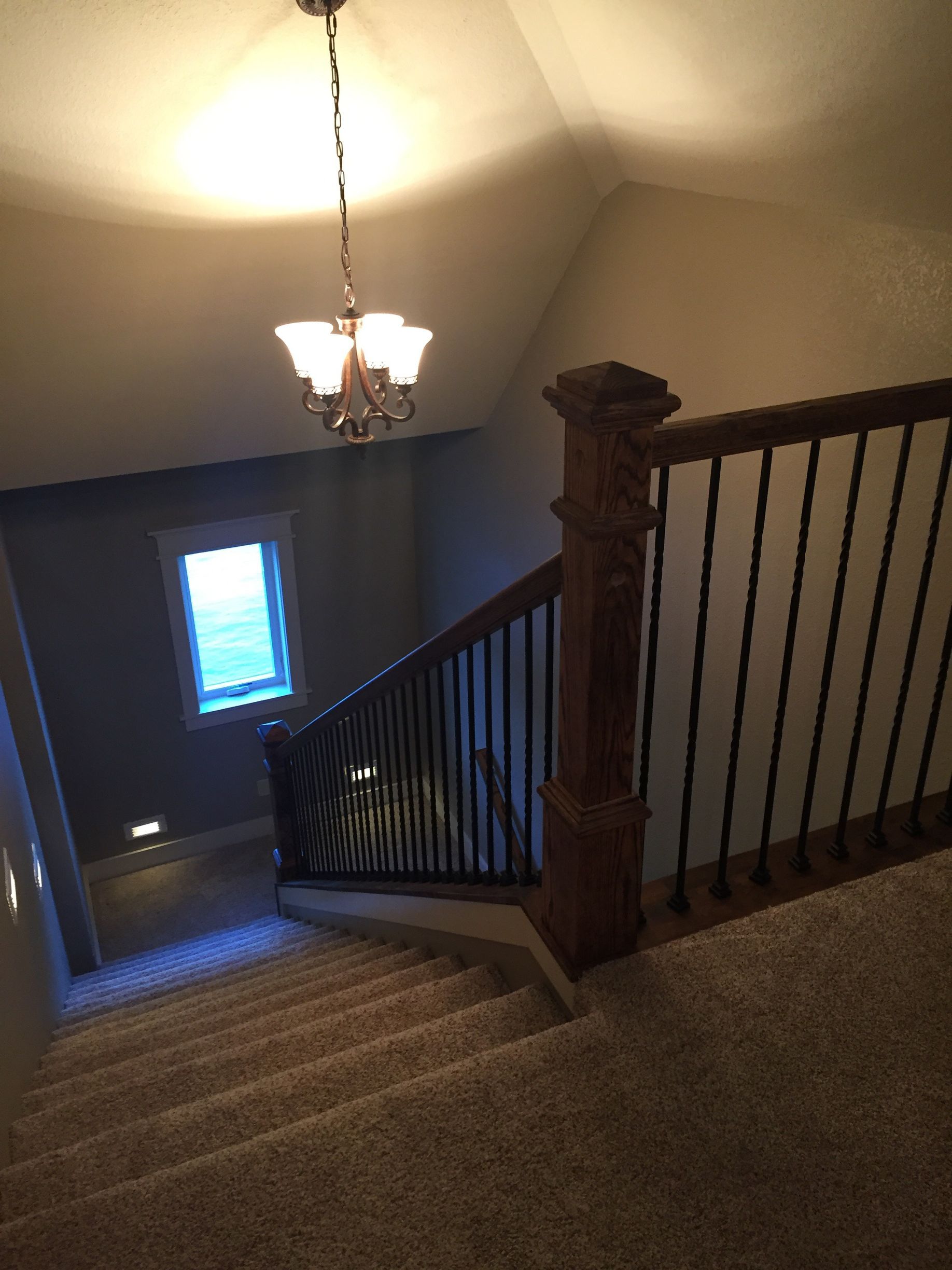 Stairway landing with carpeted stairs, dark railing, chandelier, and a small window below.