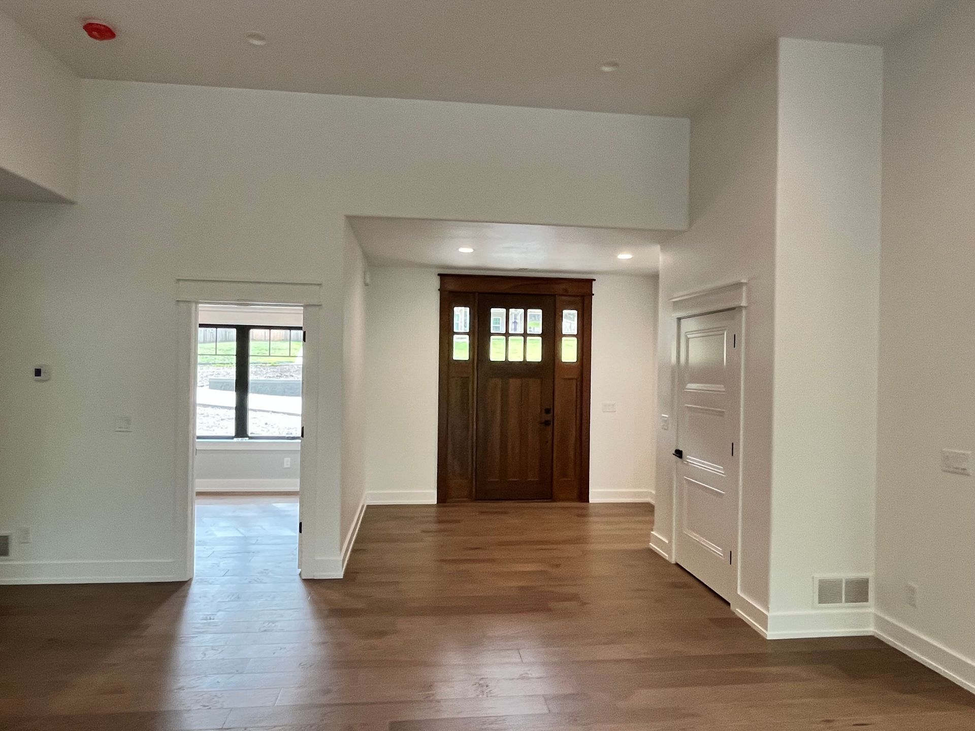 Empty living room with hardwood floors, white walls, and a wooden front door.