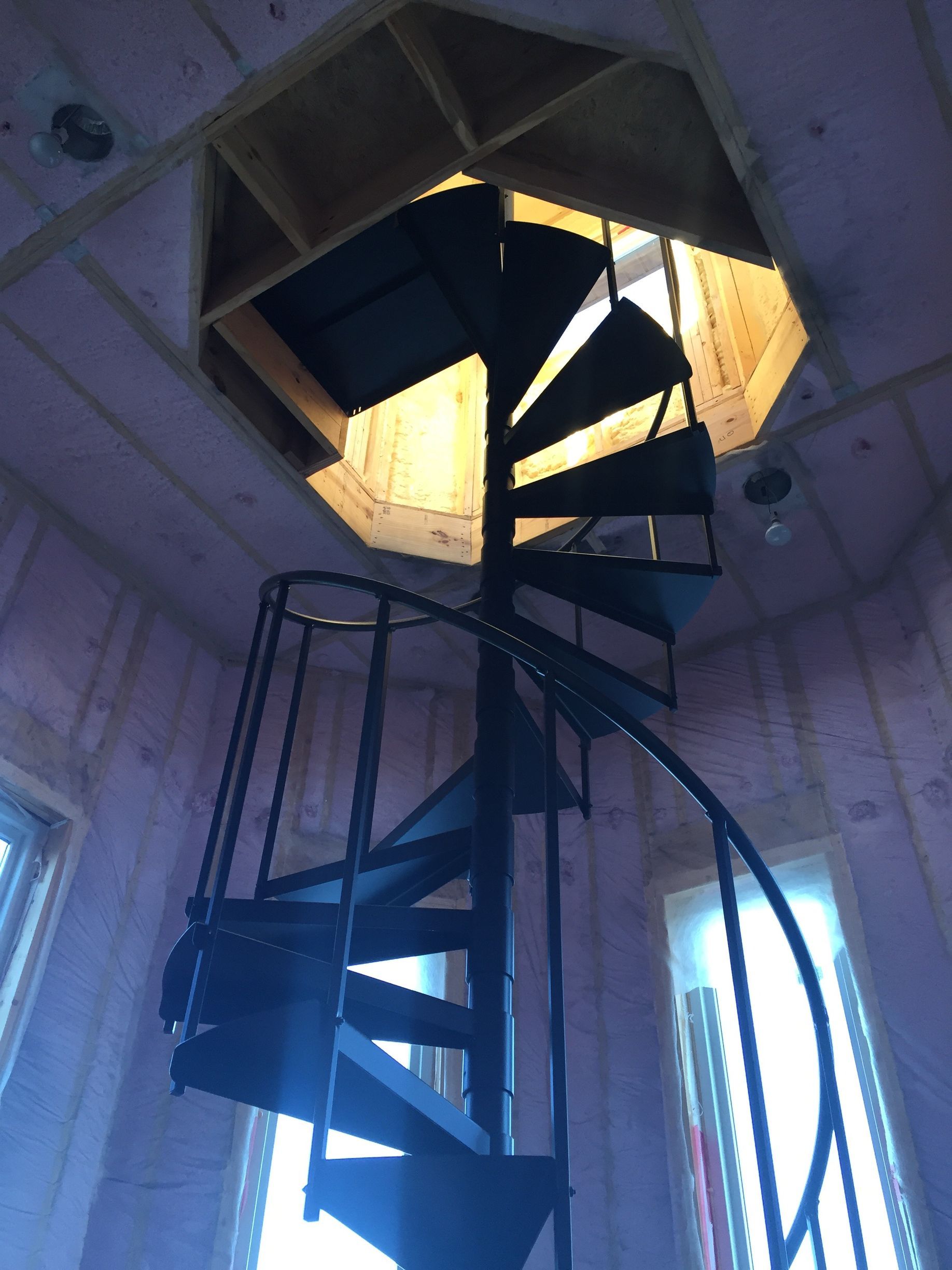 A spiral staircase rising through an octagonal tower opening, lit by daylight above.