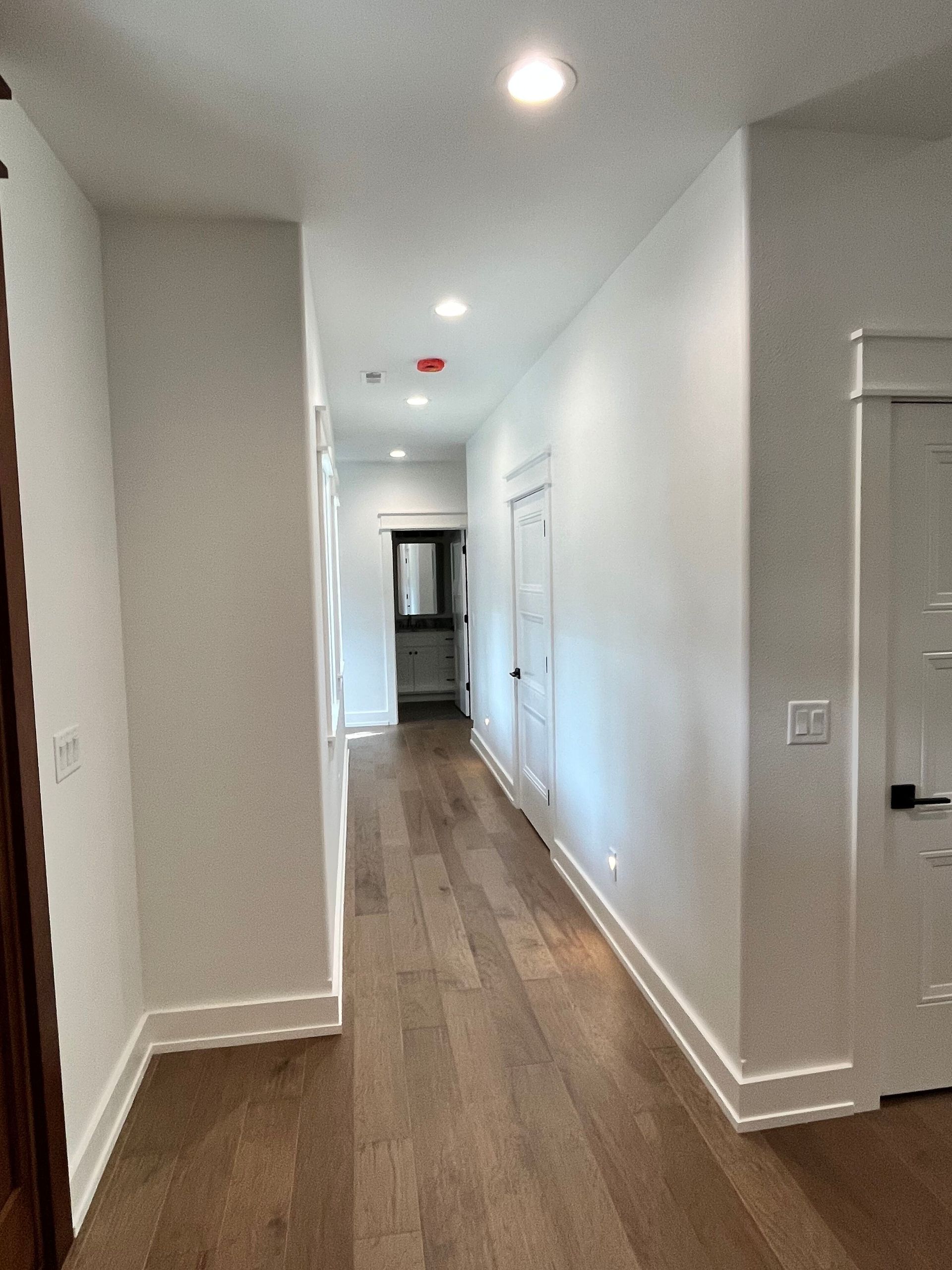 Bright hallway with white walls, wood floors, recessed lights, and doors along the right side