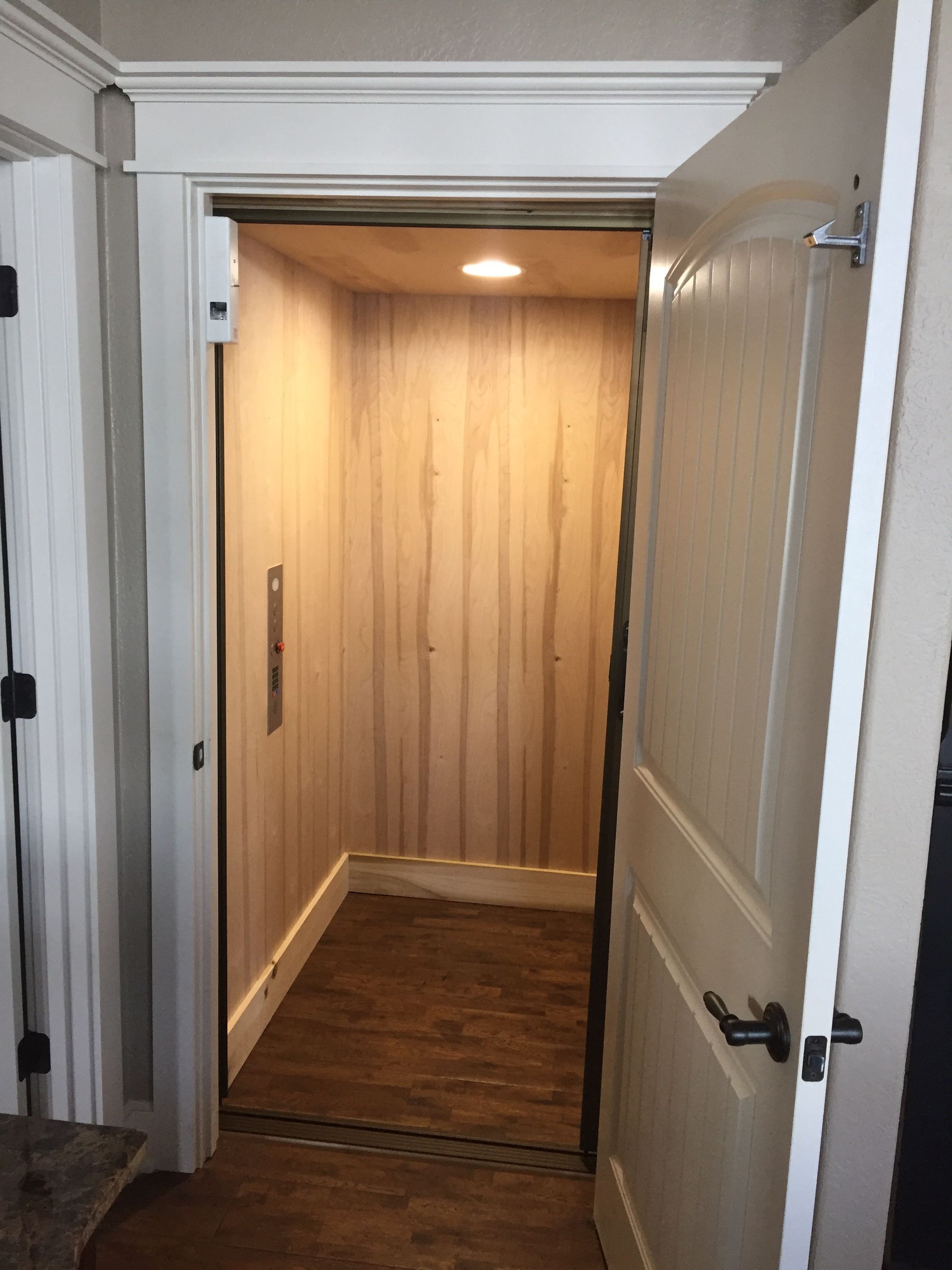 Open wooden elevator cab with warm lighting in a doorway.