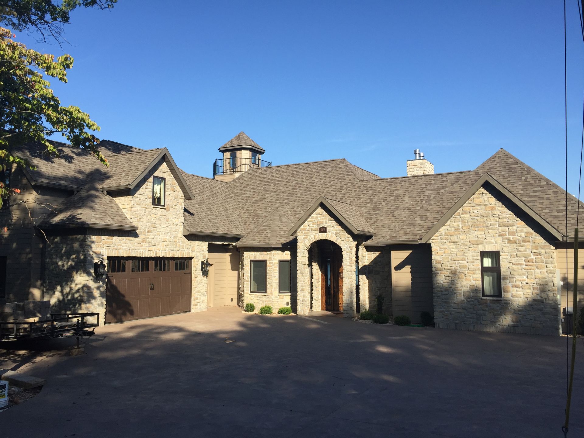 Stone house with arched entry and garage, set under a blue sky with trees casting shadows