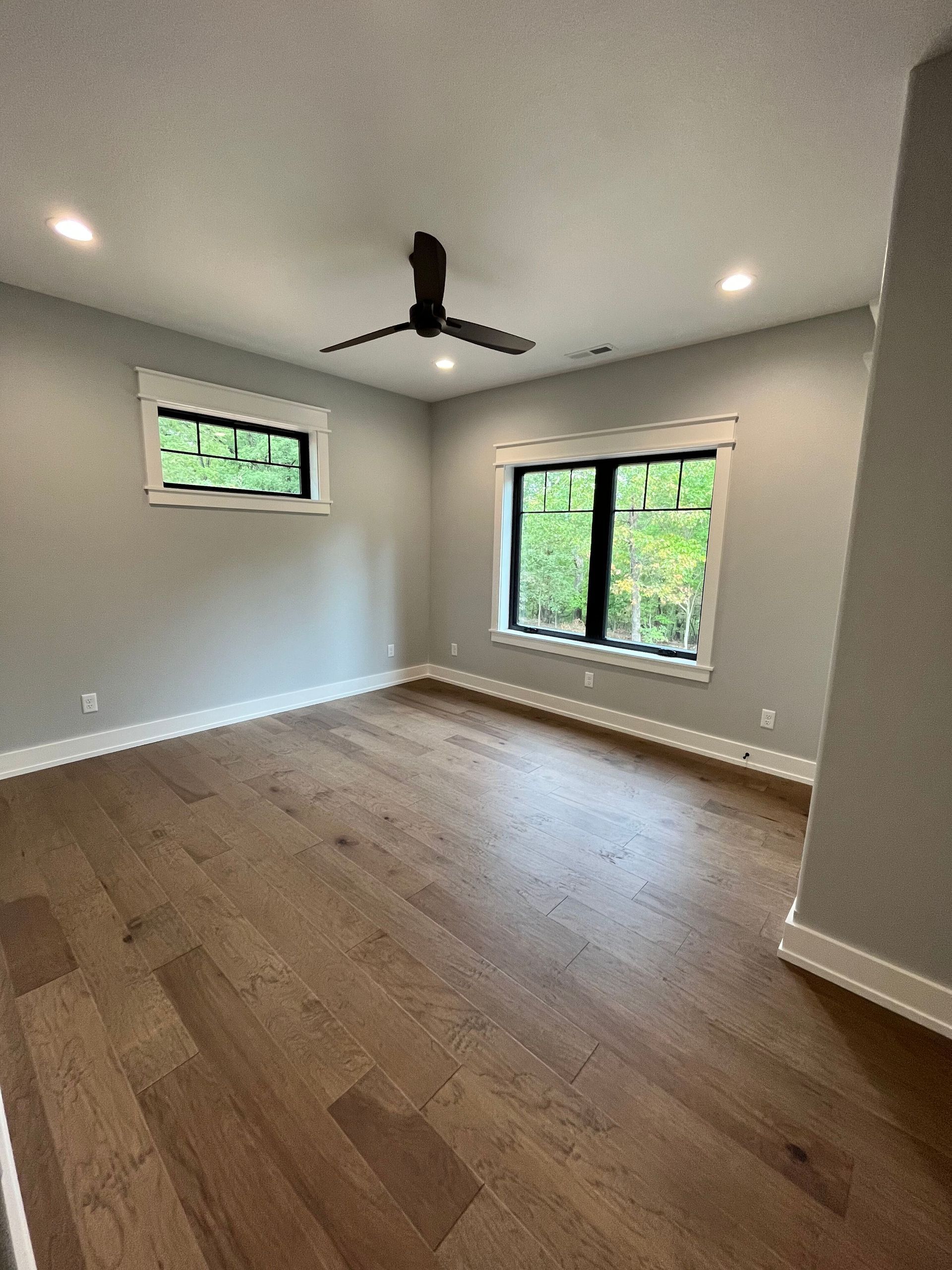 Empty modern room with wood floors, gray walls, ceiling fan, and large windows.