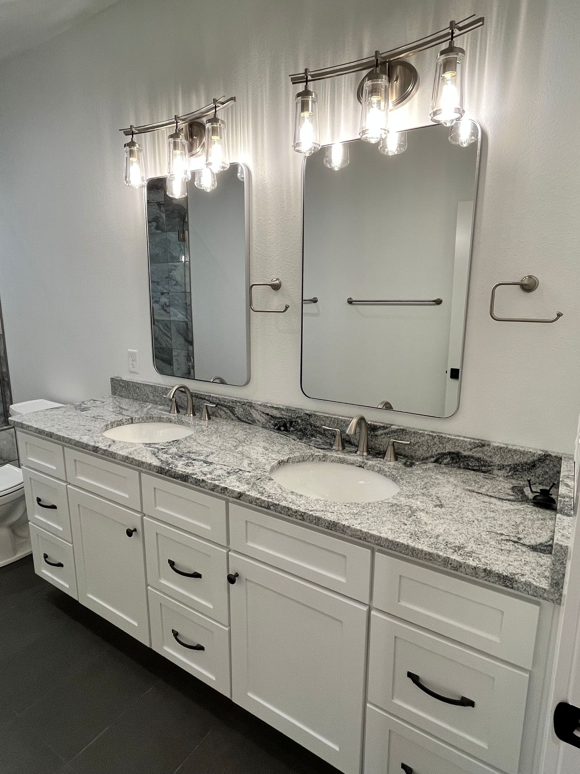 Modern bathroom vanity with granite countertop, two mirrors, wall sconces, and white cabinets