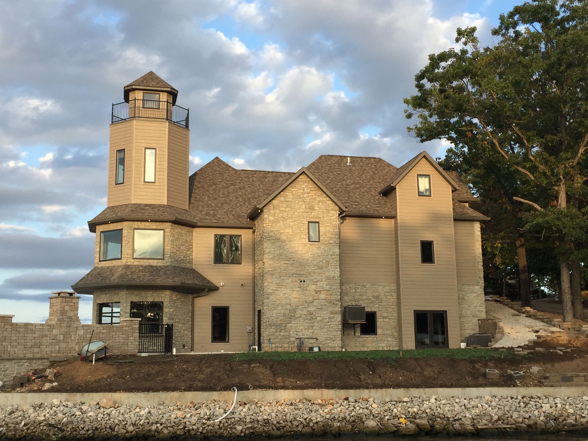 Large stone house with a tower by the water under a cloudy sky