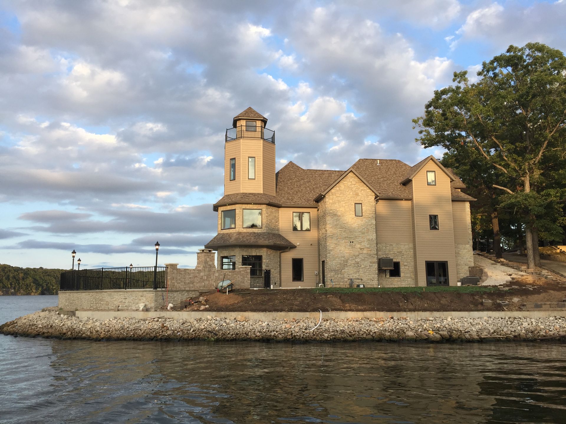 Stone waterfront house with a tower beside calm water under a cloudy sky