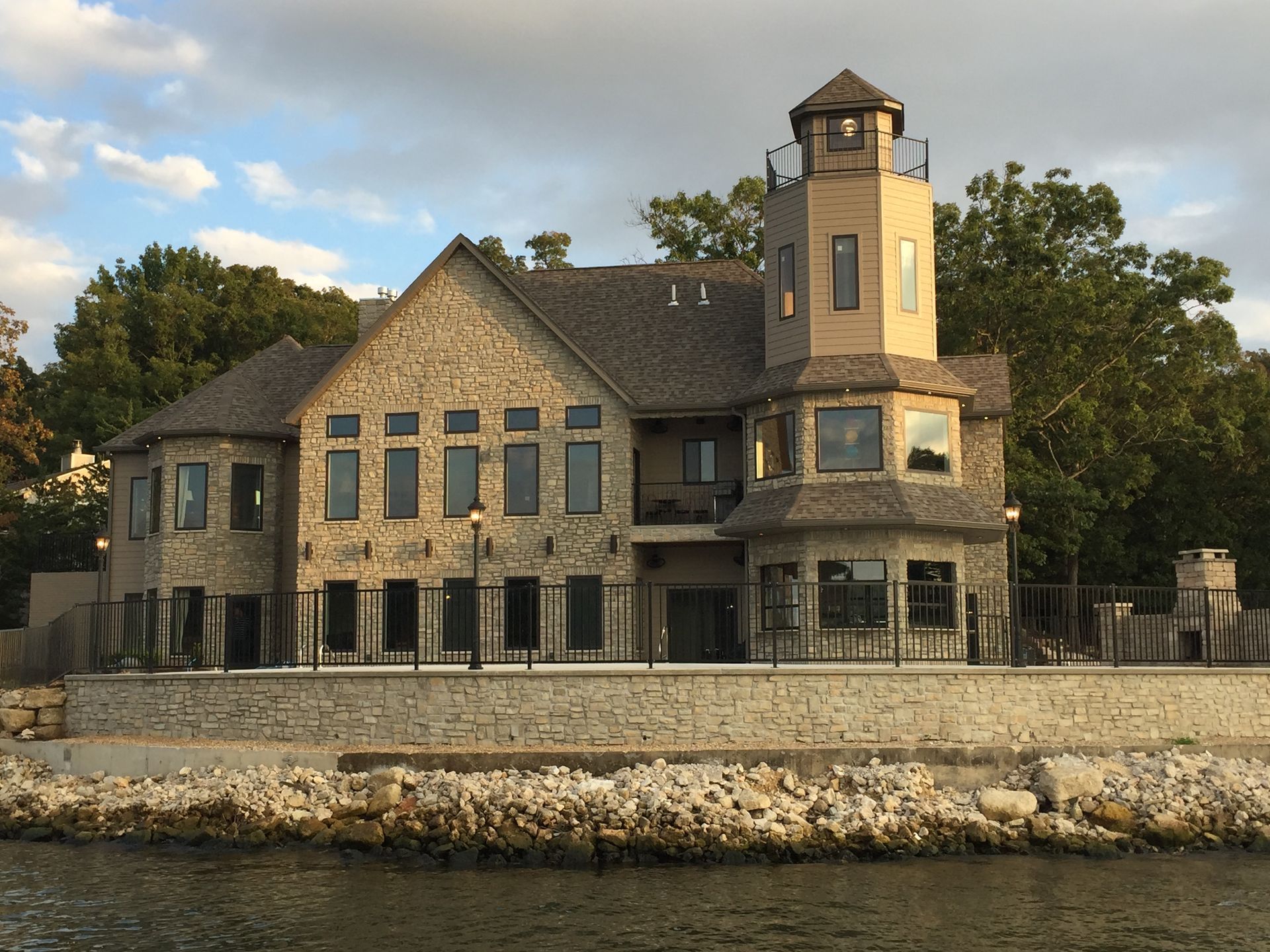 Stone lakeside house with tower behind a rock seawall at sunset
