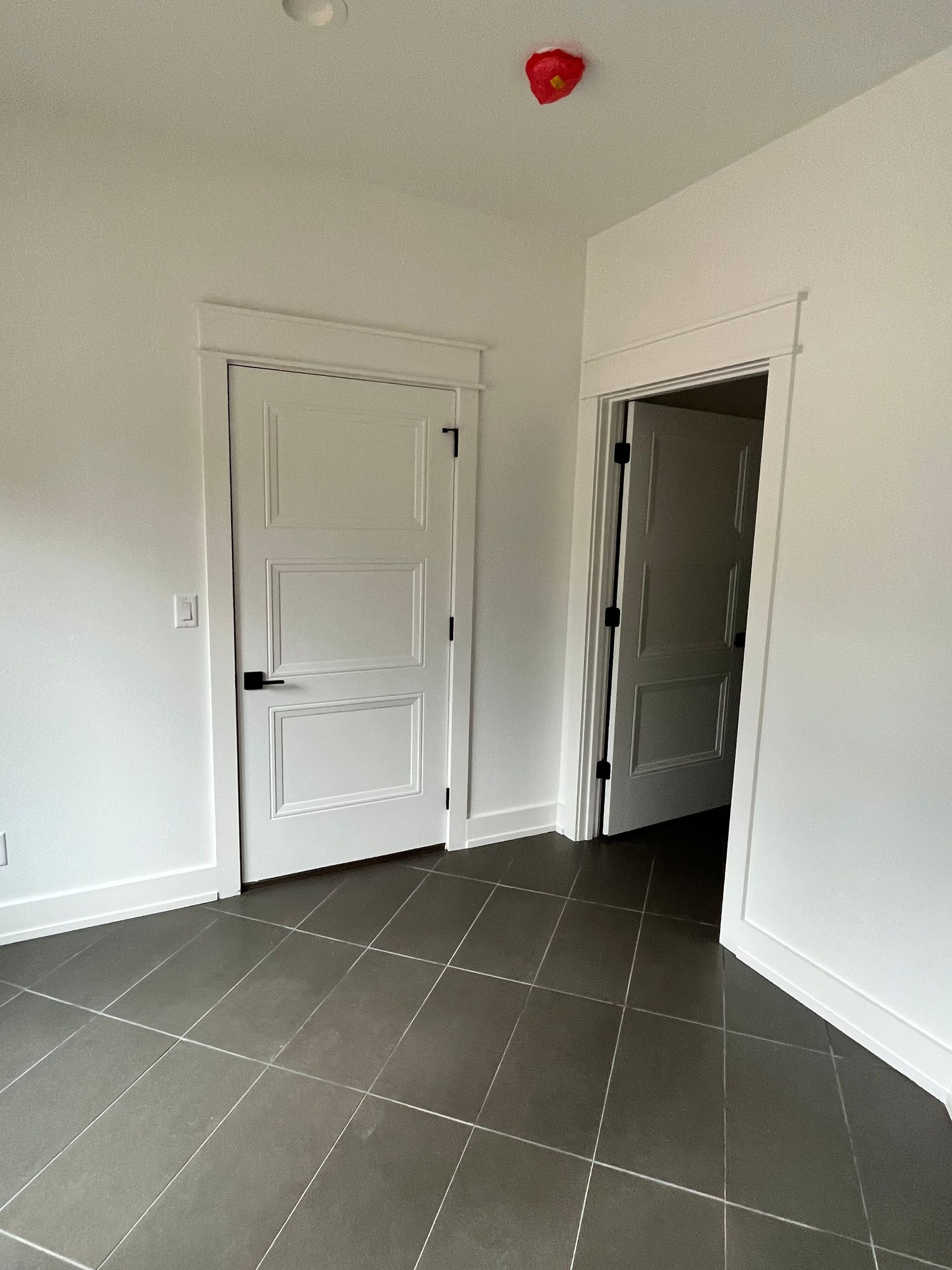 Empty white room with two doors, dark tiled floor, and a red ceiling fixture.