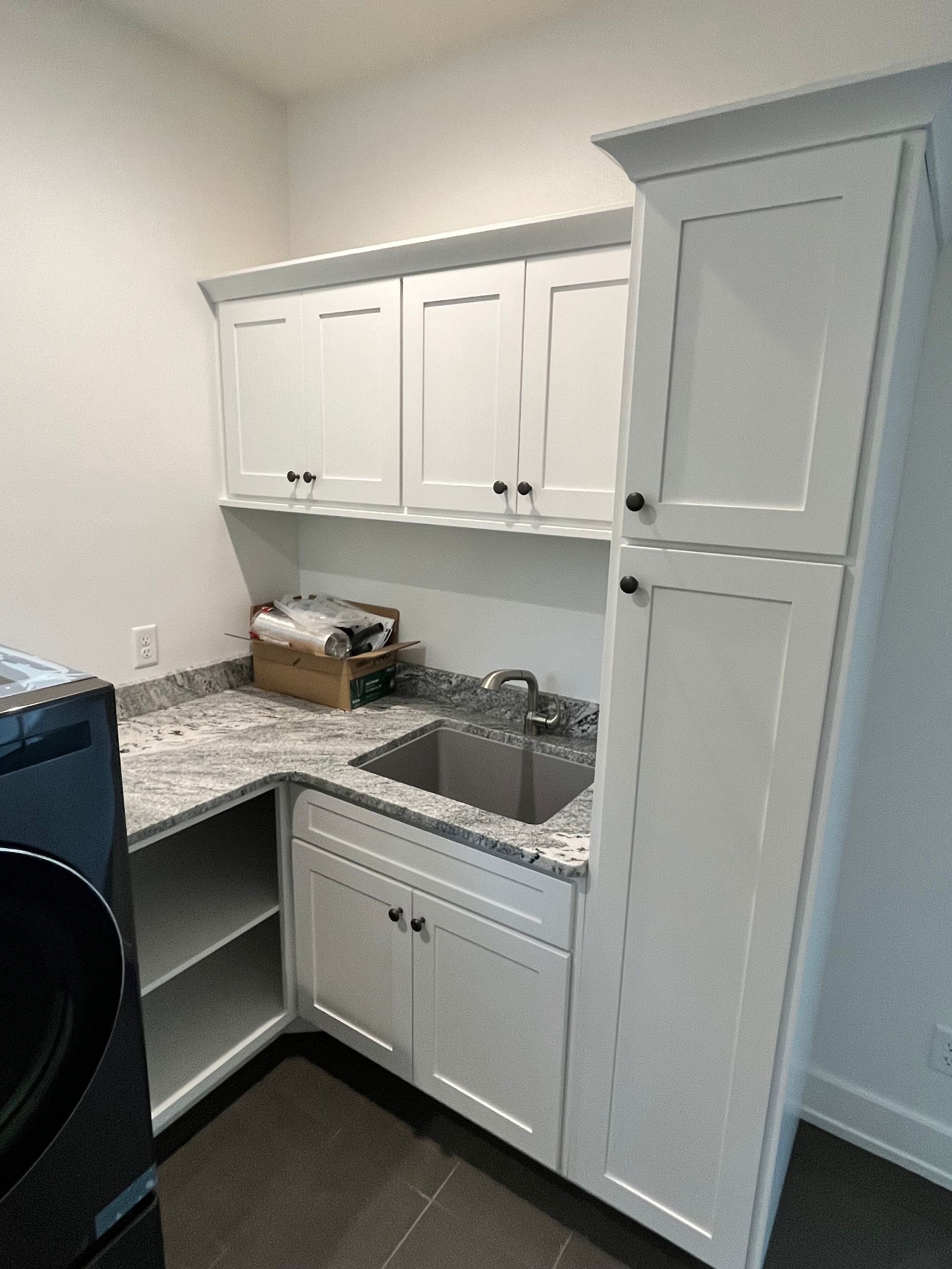 Small kitchen with white cabinets, gray countertops, sink, and tall pantry cabinet.