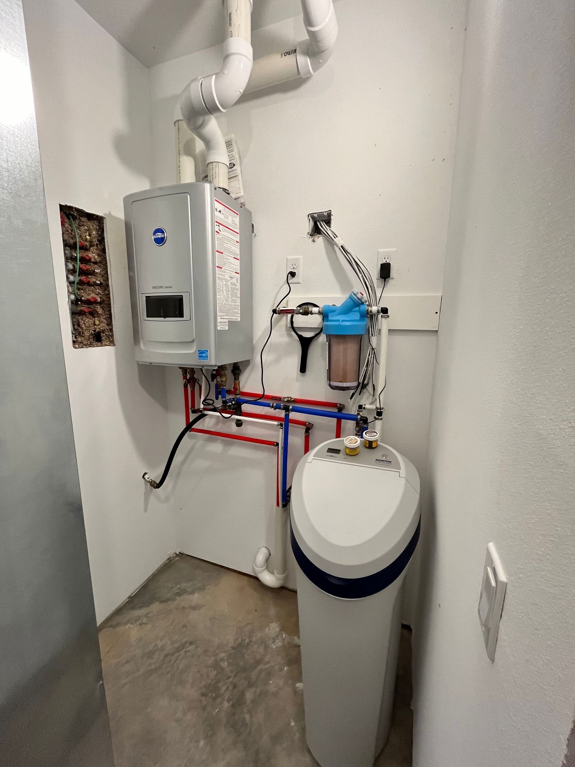 Utility room with a wall-mounted water heater, pipes, and a large white water softener tank
