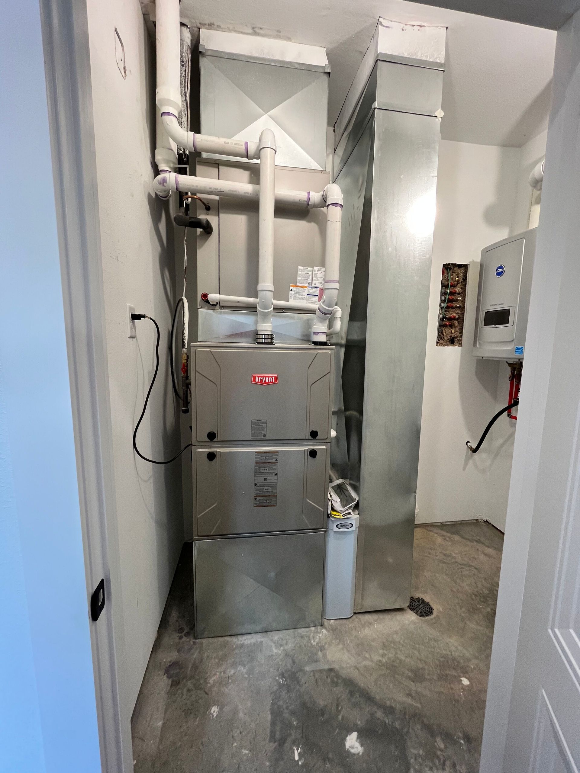 Utility closet with a gray furnace, white pipes, and ductwork in a narrow hallway.