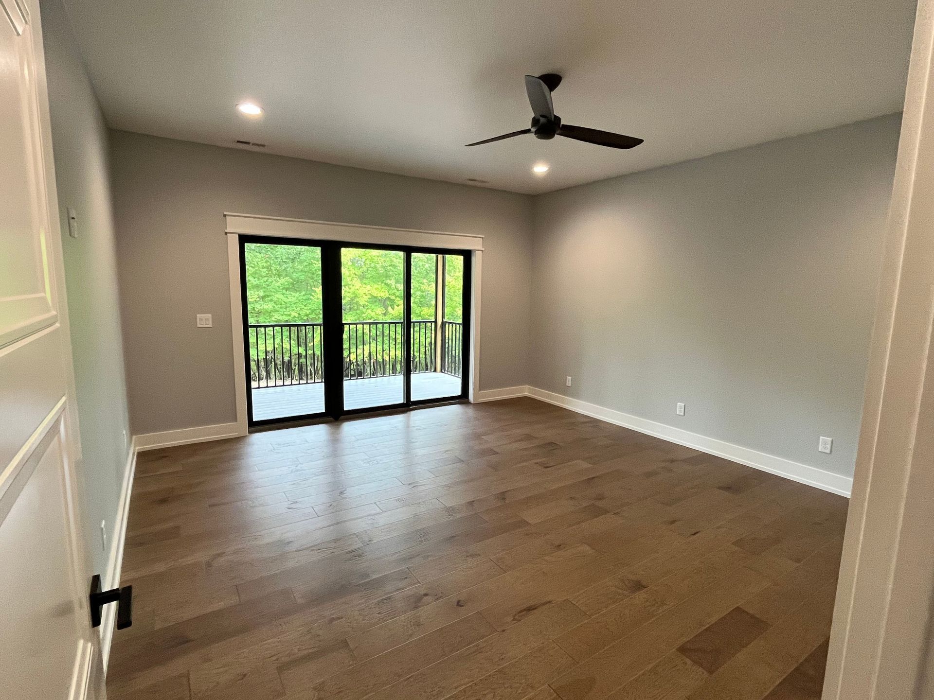 Empty living room with wood floors, ceiling fan, and sliding glass doors to a balcony.