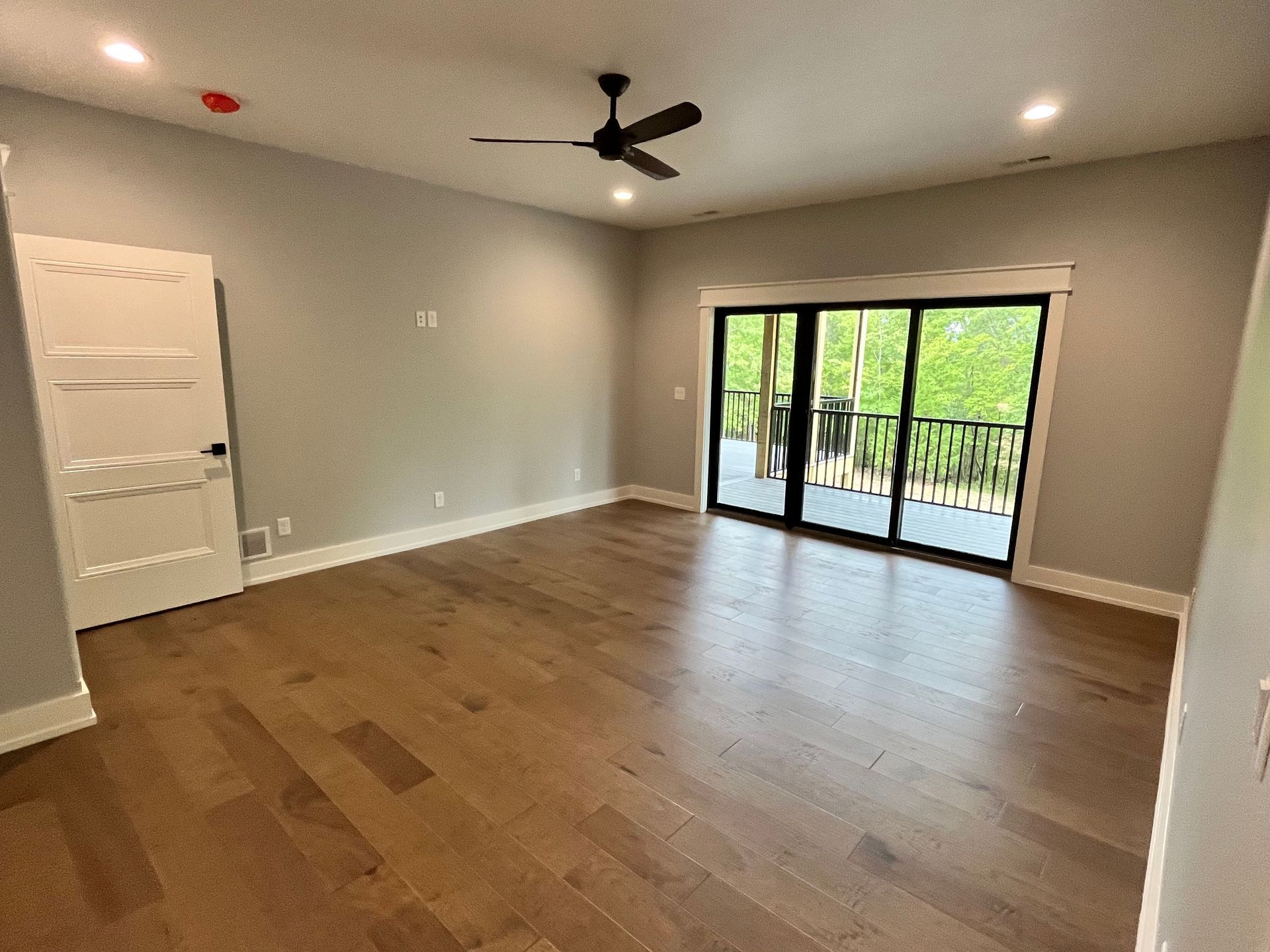 Empty room with wood floors, gray walls, ceiling fan, and sliding glass doors to a balcony.
