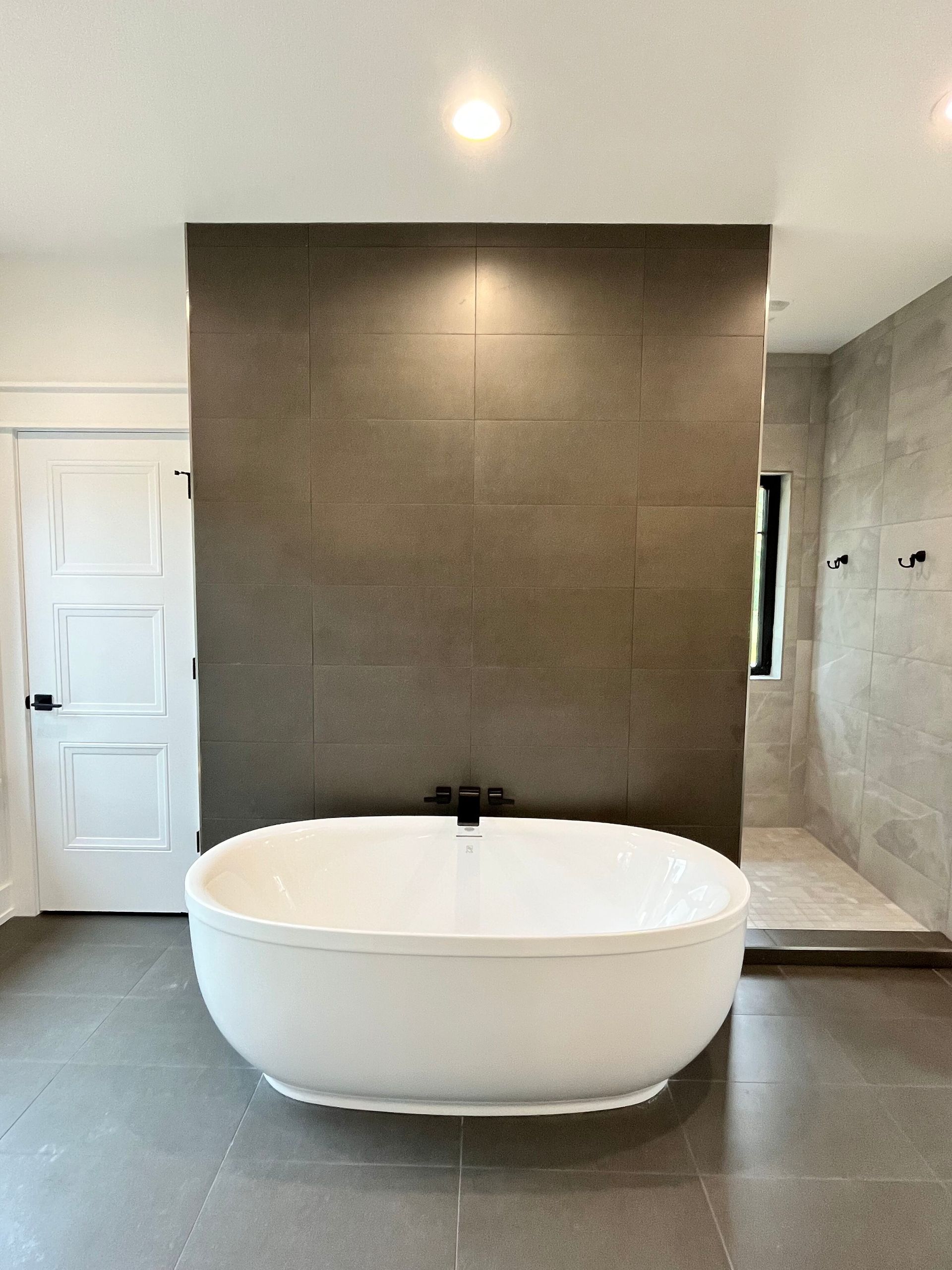 Modern bathroom with a freestanding oval tub before a dark tile accent wall
