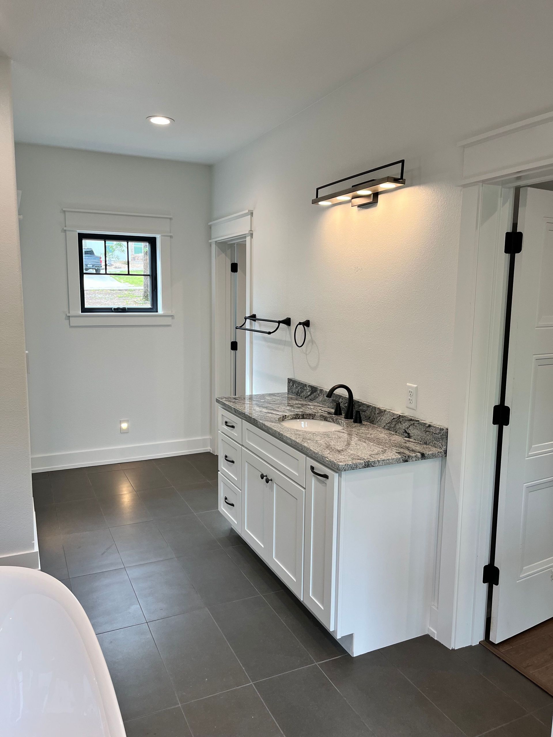 Modern bathroom with white vanity, granite countertop, dark tile floor, and window.
