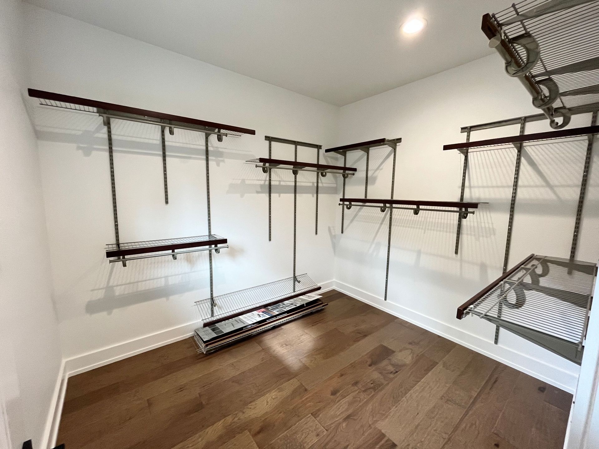 Empty walk-in closet with white walls, wood floor, and hanging wire shelves and racks.